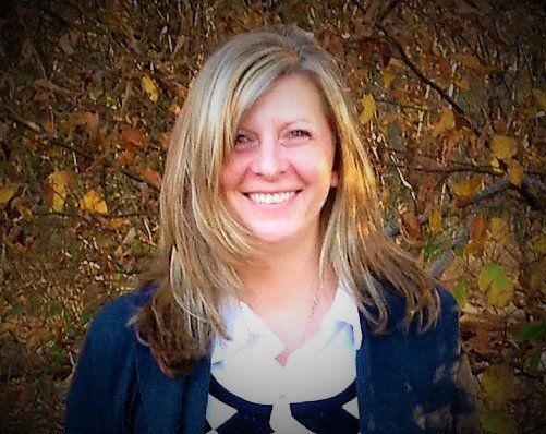 A woman is smiling in front of a tree with leaves