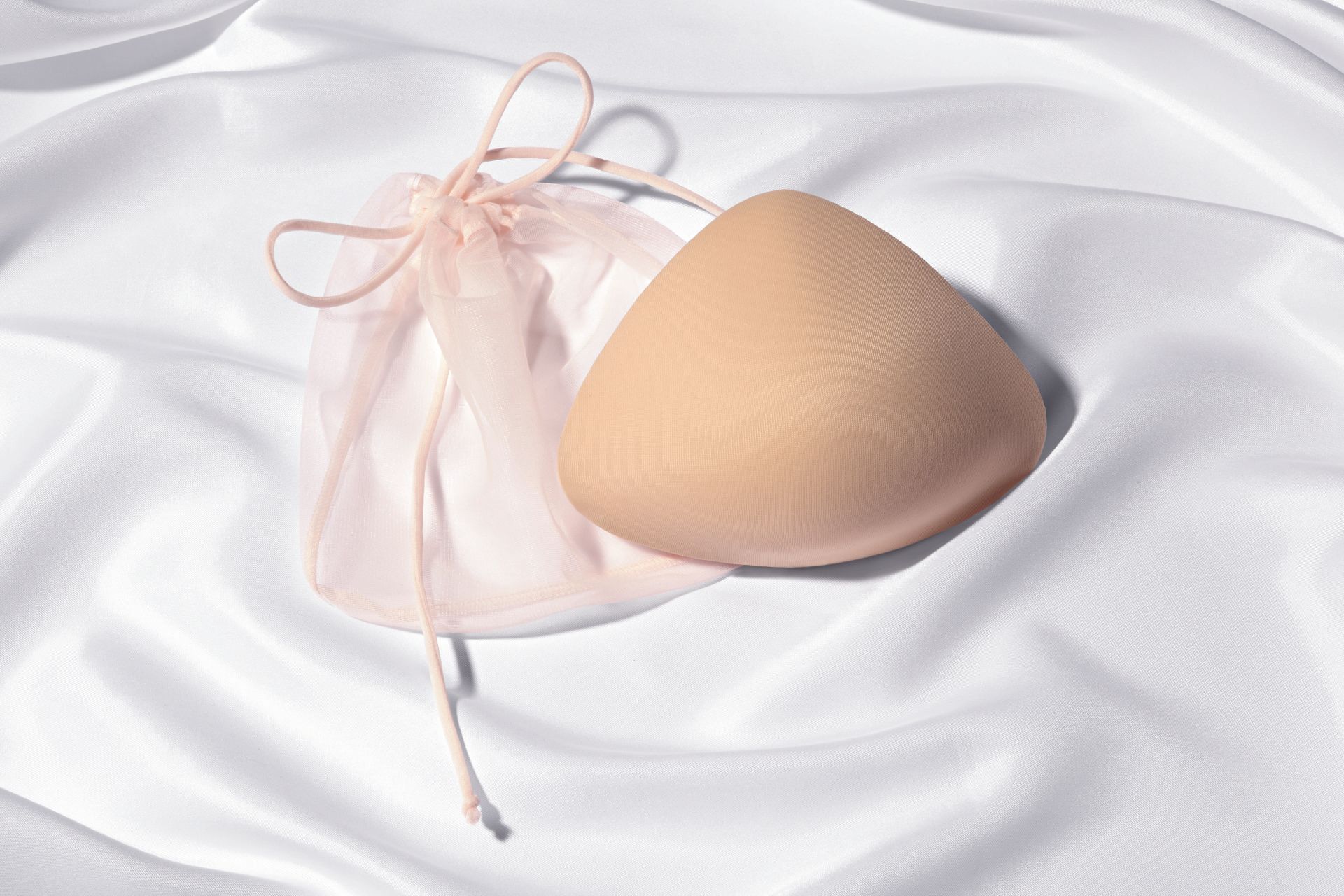 A breast form is sitting on a white cloth next to a pink bag.
