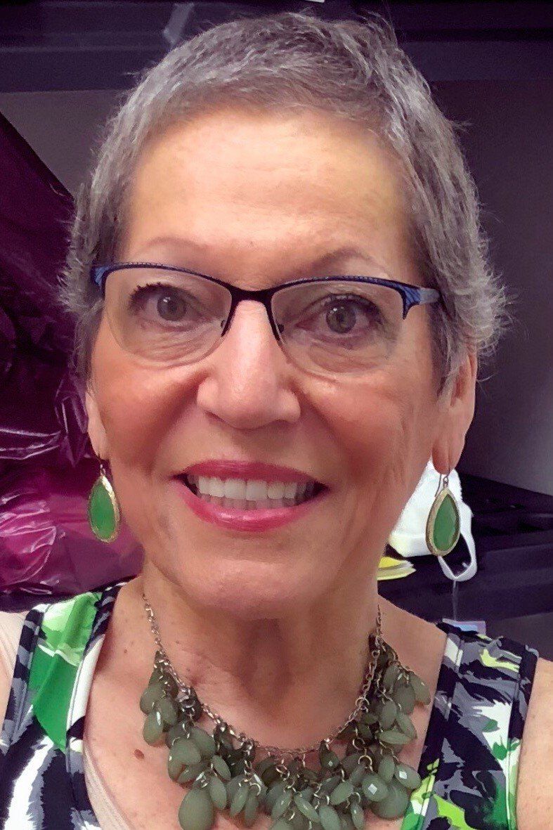 A woman wearing glasses and a green necklace smiles for the camera