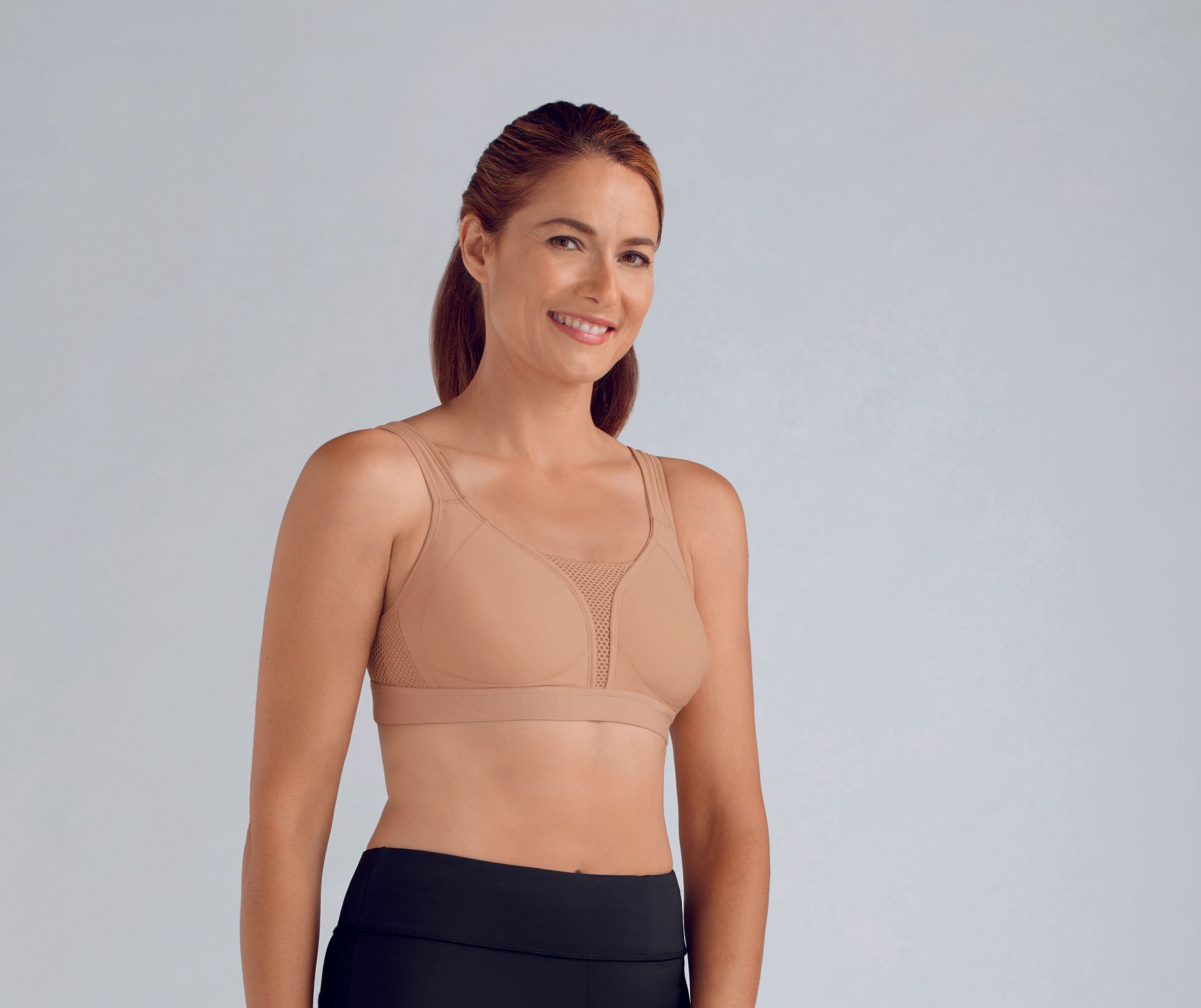 A woman wearing a sports bra and black pants is smiling.
