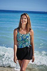 A woman in a swimsuit and skirt is standing on the beach.