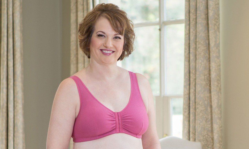 A woman wearing a pink bra is standing in front of a window.