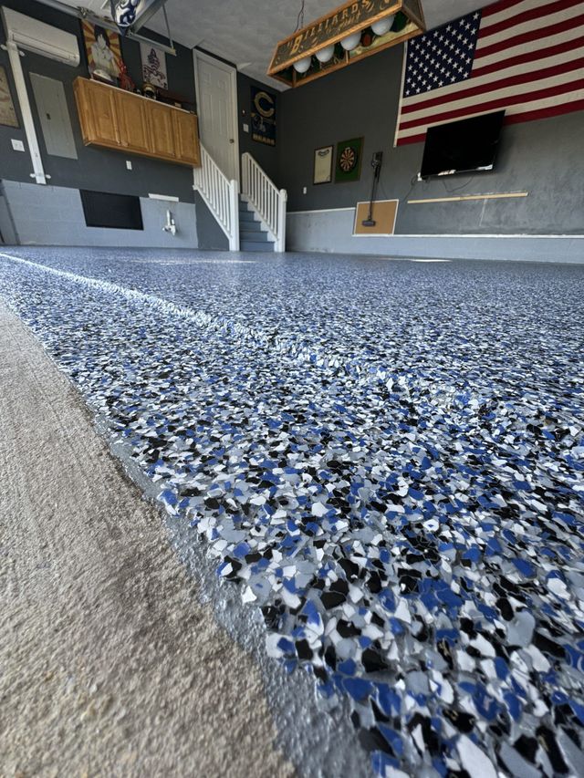 Garage with blue-speckled epoxy floor, gray walls, stairs, and an American flag on the wall.