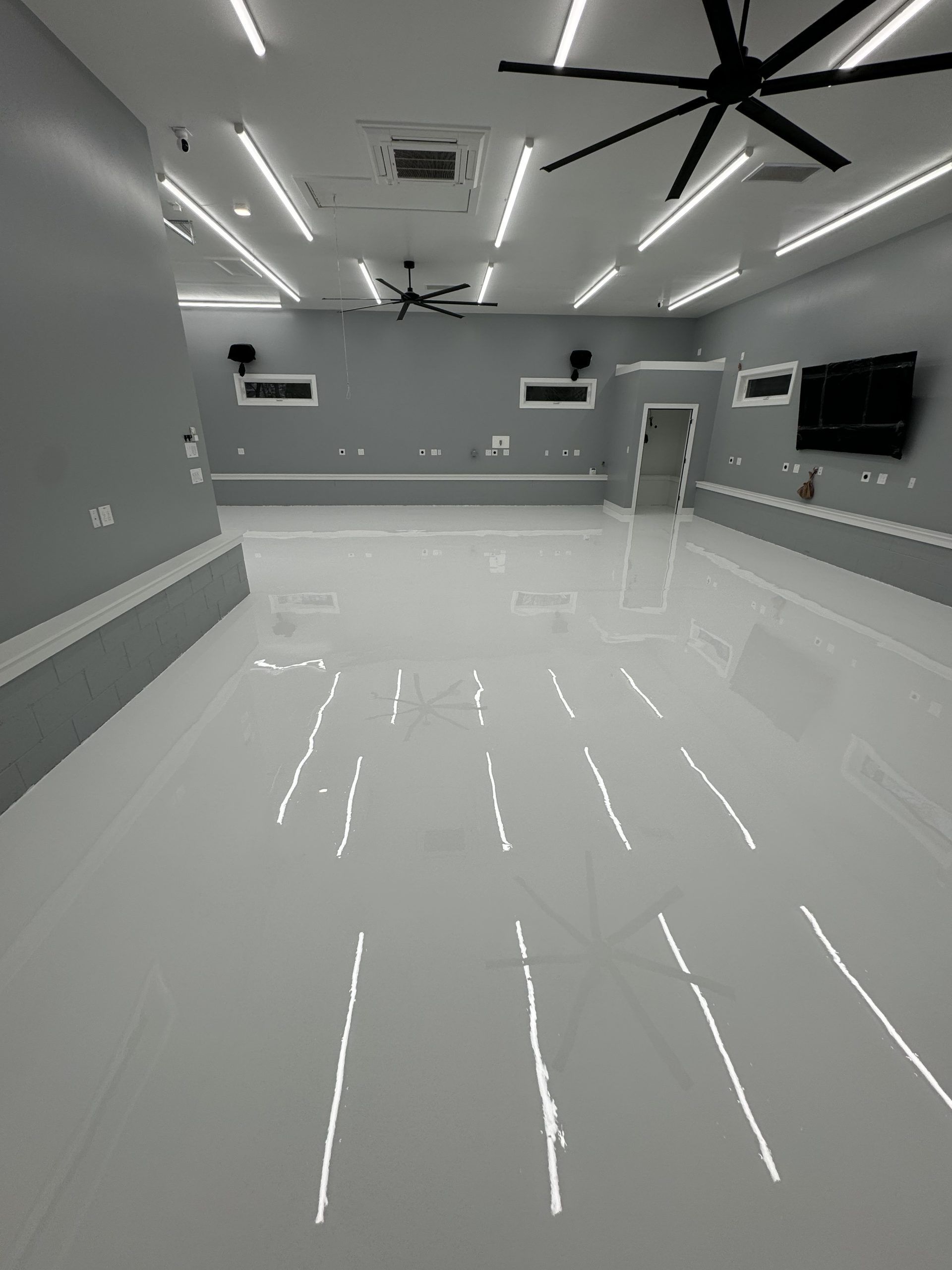 Empty modern room with glossy white floors, gray walls, ceiling fans, and wall-mounted TVs