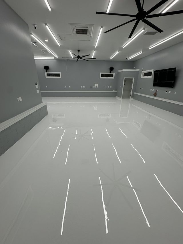 Empty modern room with glossy floor, gray walls, ceiling fans, recessed lights, and wall-mounted screens.