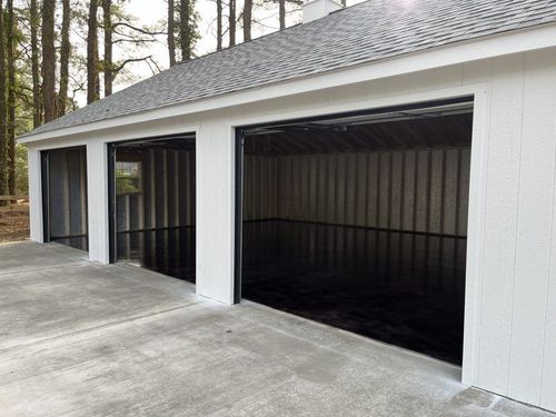 Three-car garage with white exterior and open dark interior beside a concrete driveway