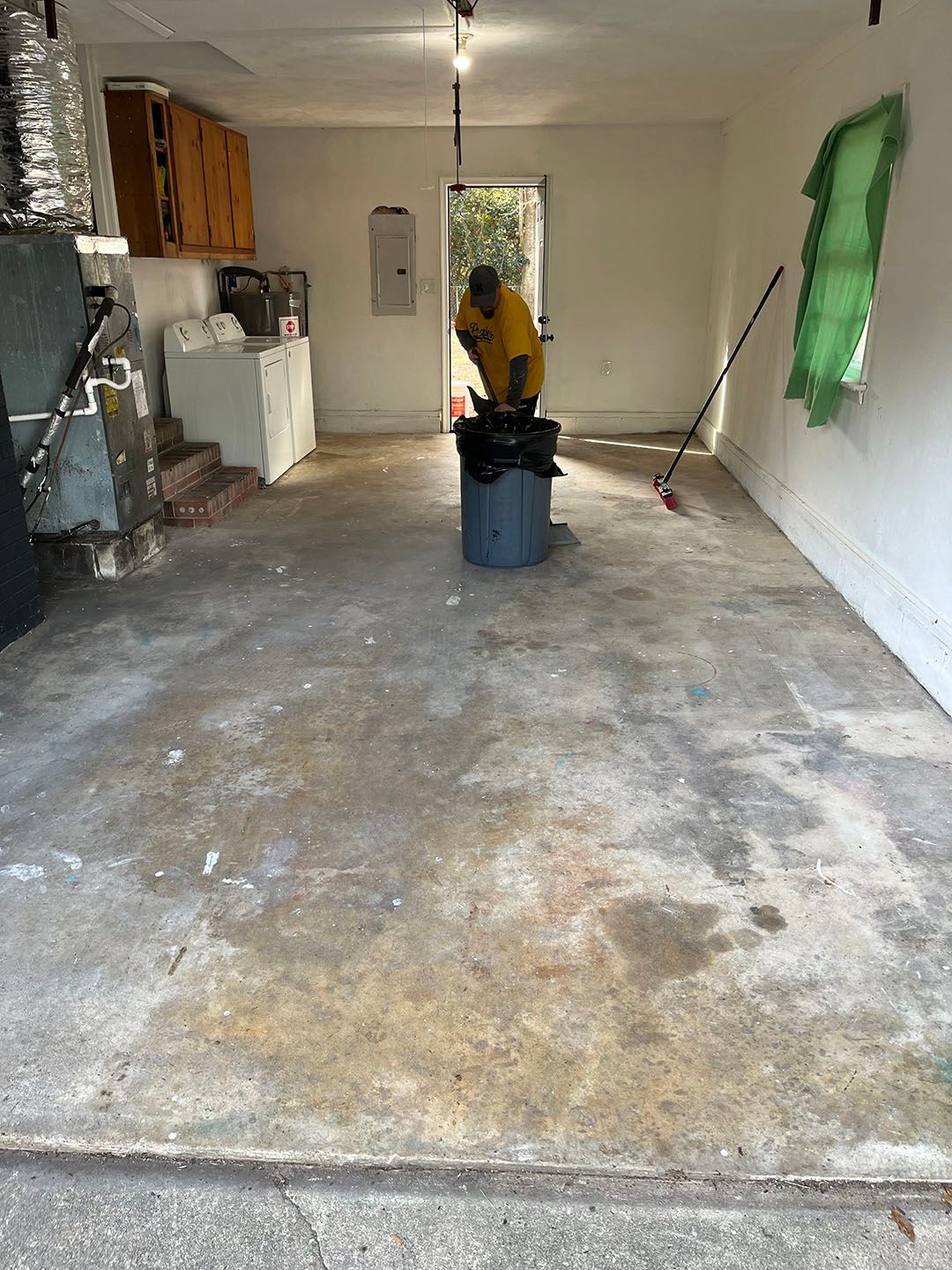 Empty garage interior with a person in a yellow shirt cleaning the concrete floor with a vacuum.