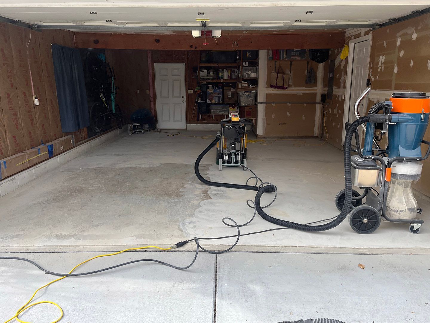 Garage interior with concrete floor, exposed insulation, tools, and a pressure washer hose across the ground.