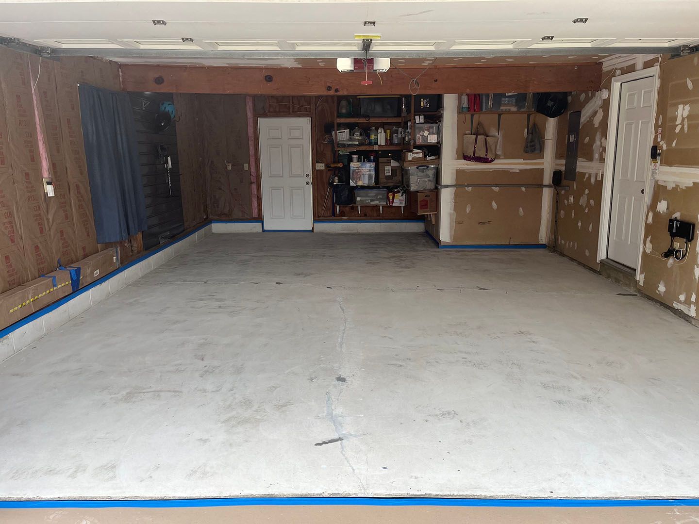 Empty unfinished garage with a concrete floor, exposed walls, and storage shelves at the back.