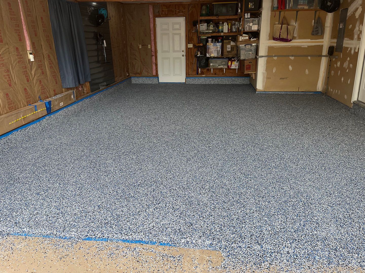 Empty unfinished garage with a speckled gray floor and cardboard boxes stacked along the walls.
