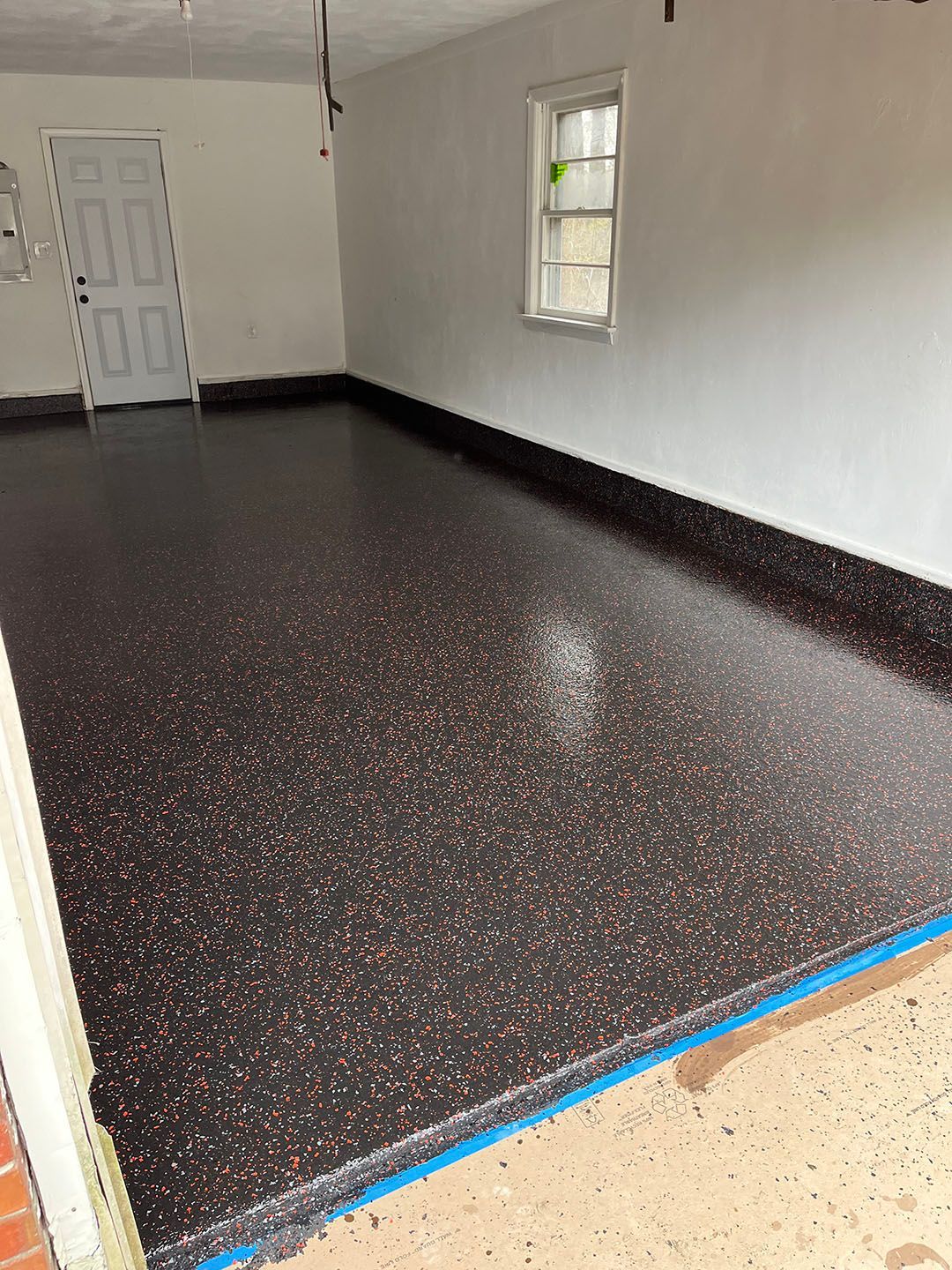 Empty room with black speckled epoxy floor, white walls, and a window and door.