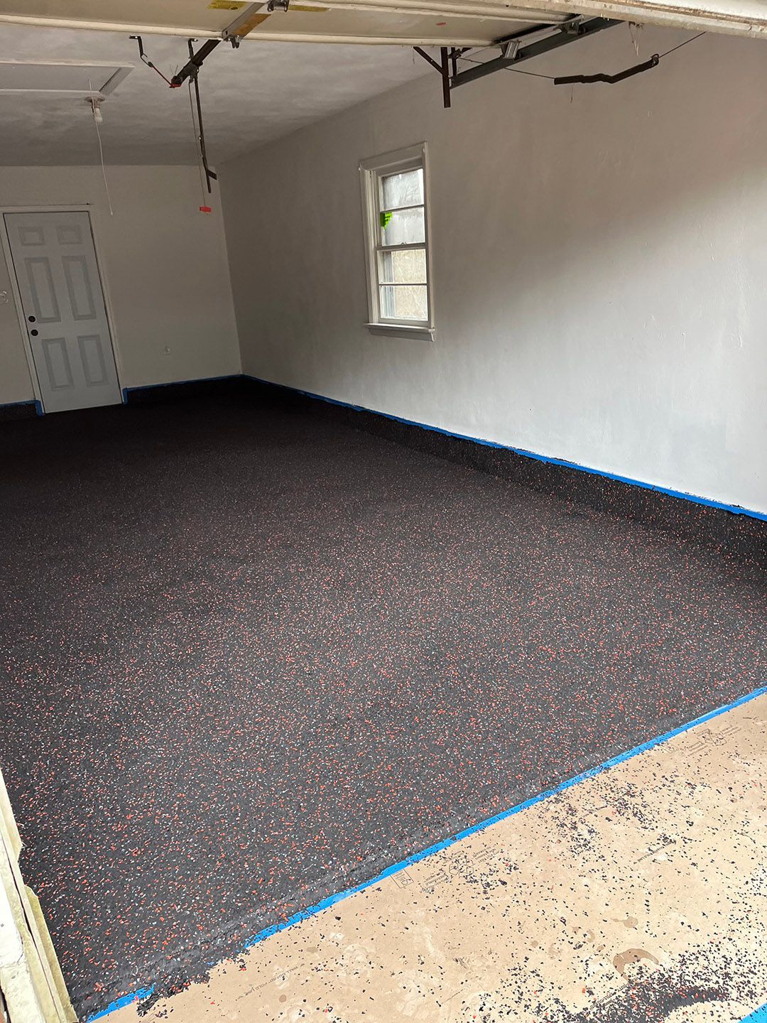 Empty room with black carpet, white walls, a small window, and blue painter’s tape along the floor edges.