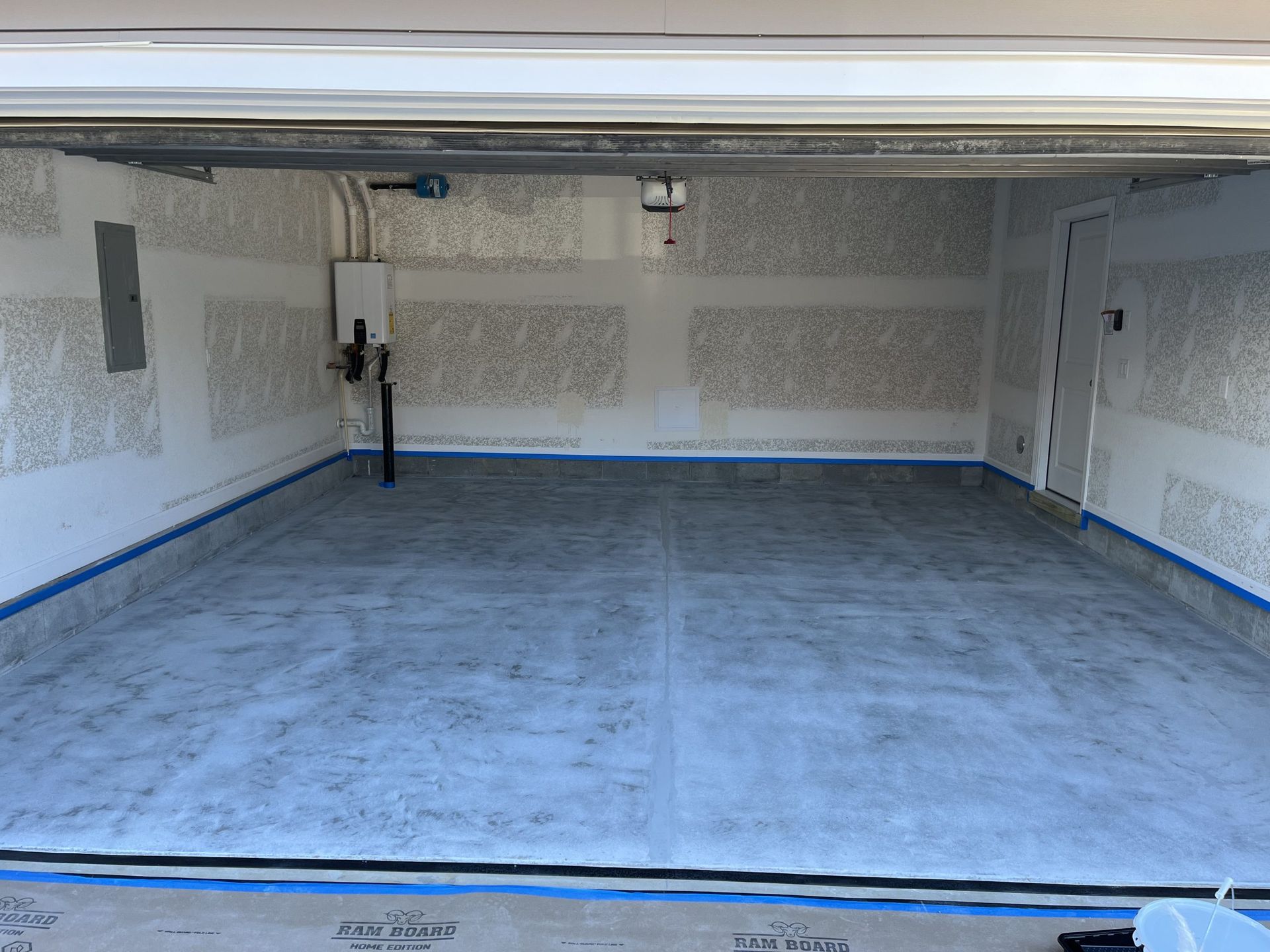 Empty garage interior with a blue floor covering and white walls under fluorescent lighting