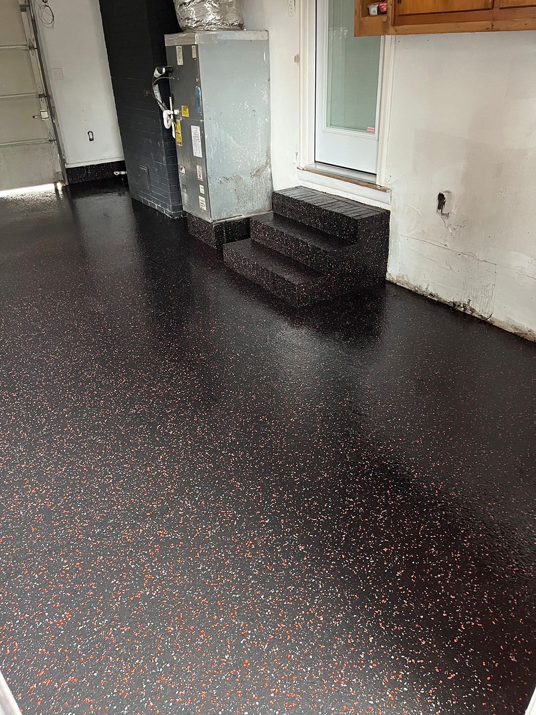 Empty room with glossy black speckled floor, white walls, and a small raised platform by a door