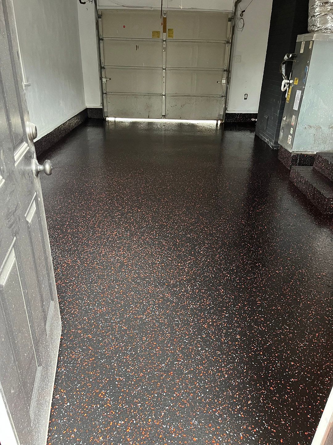 Empty garage with dark speckled floor, white walls, and a closed door at the back.