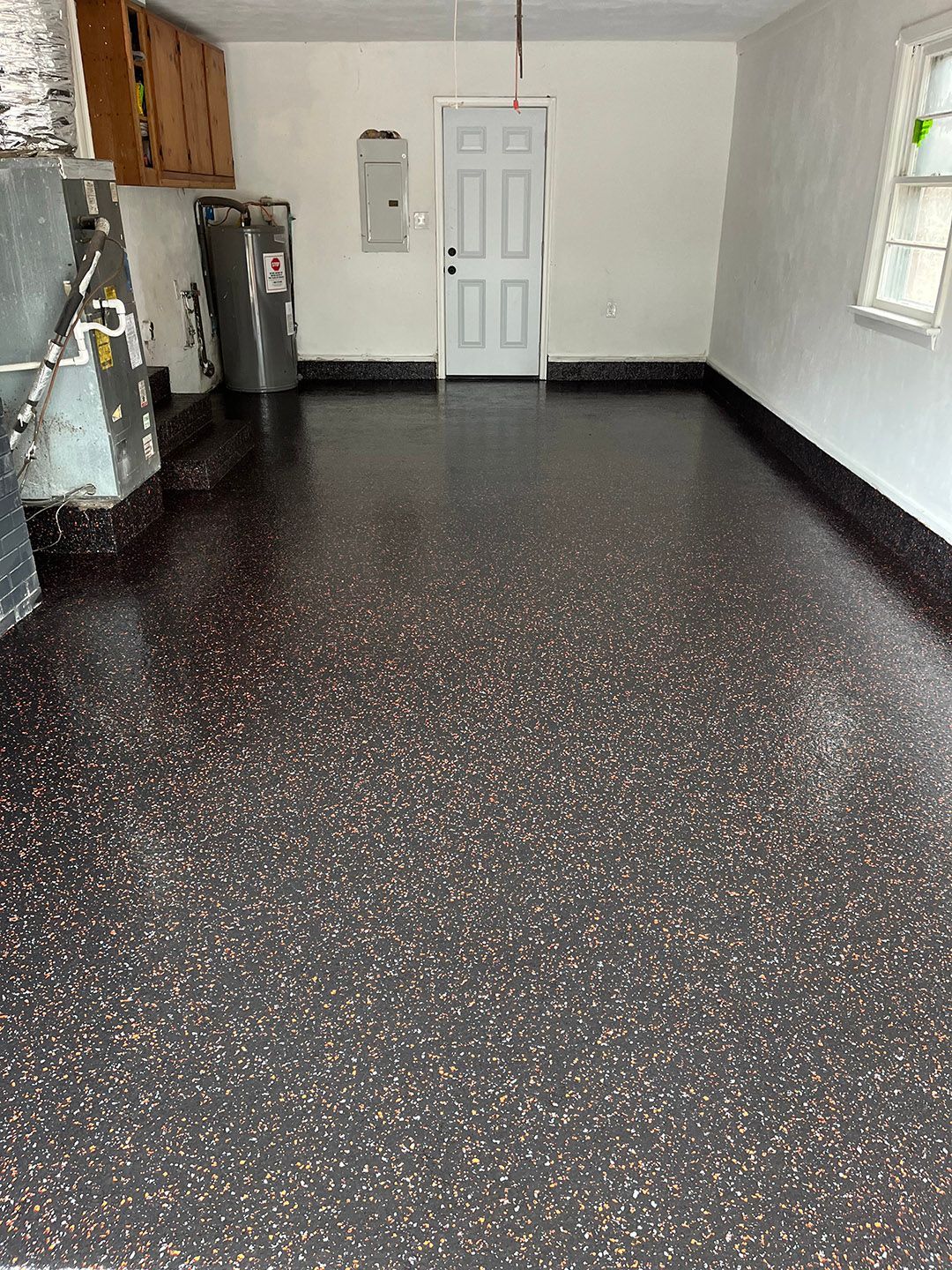 Empty room with dark speckled floor, white door, cabinets, and a window on the right.