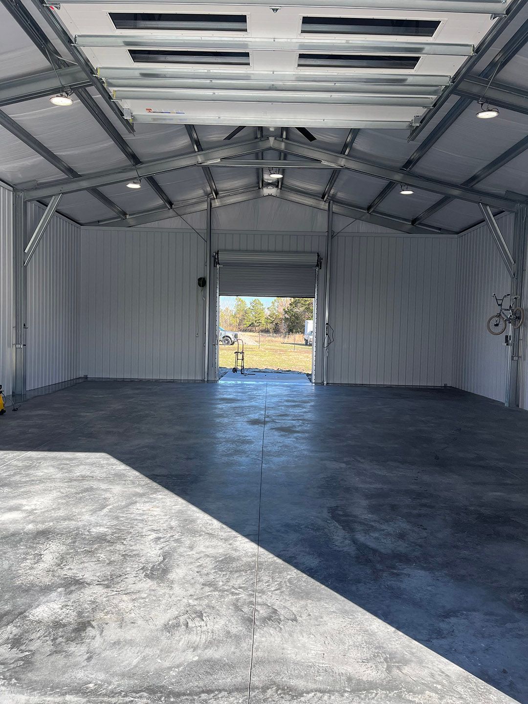 Empty metal shed interior with open doorway and a concrete floor, lit by daylight