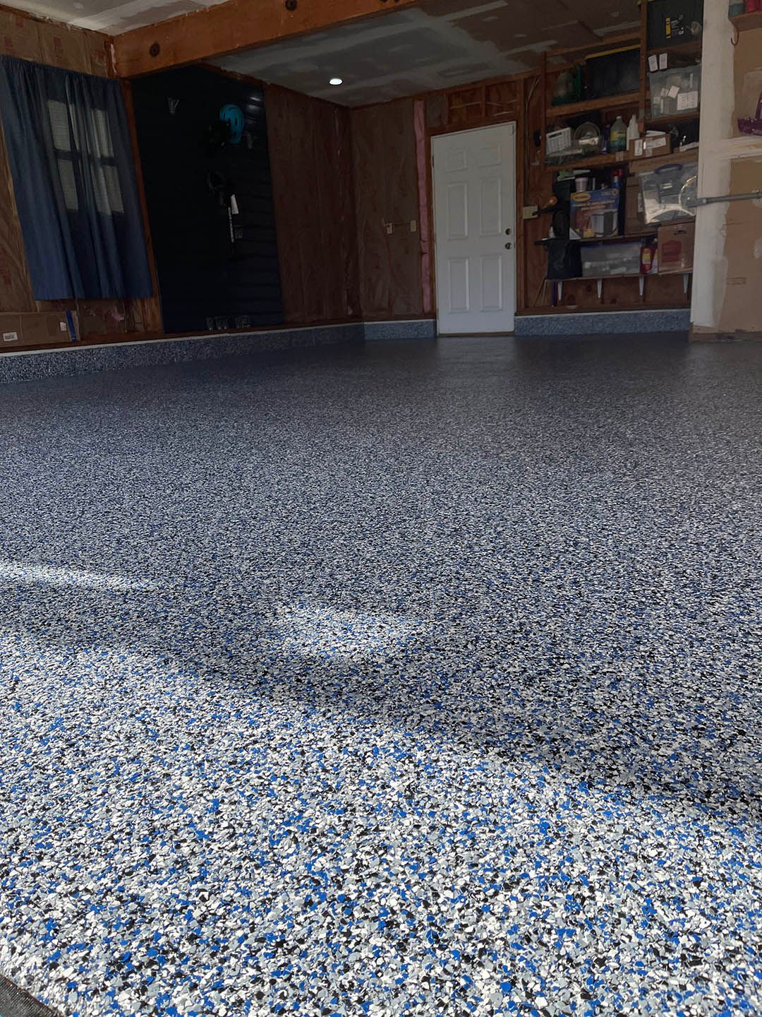 Empty garage with speckled epoxy floor and storage shelves along the back wall.