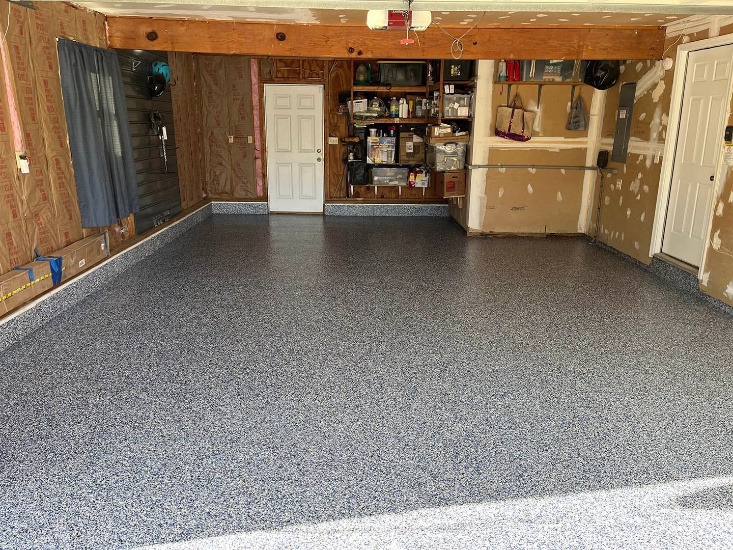 Empty garage with speckled epoxy floor, wood walls, shelves, and storage cabinets.