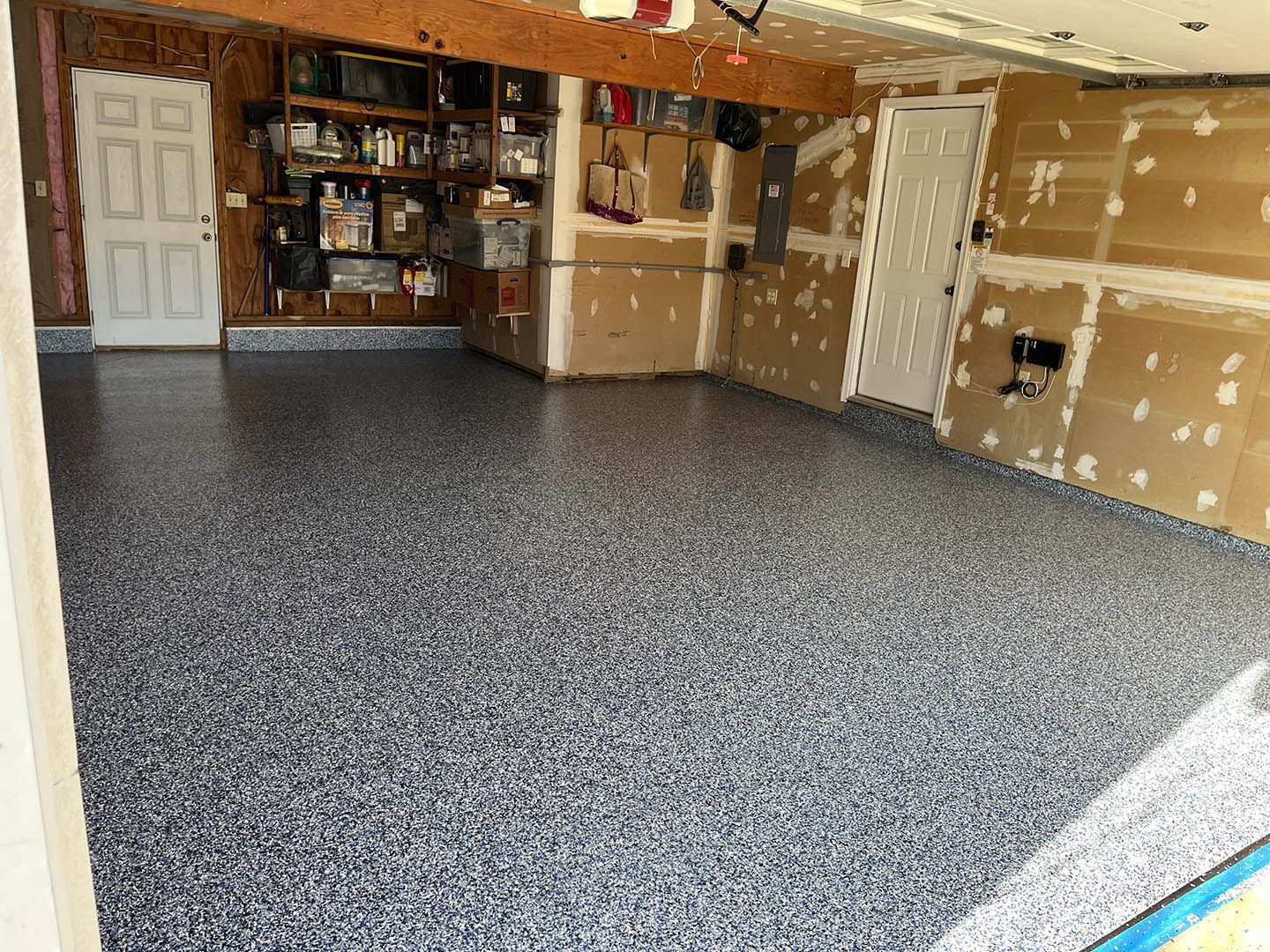 Garage with gray speckled floor, white walls, cardboard boxes, and shelves along the back wall.
