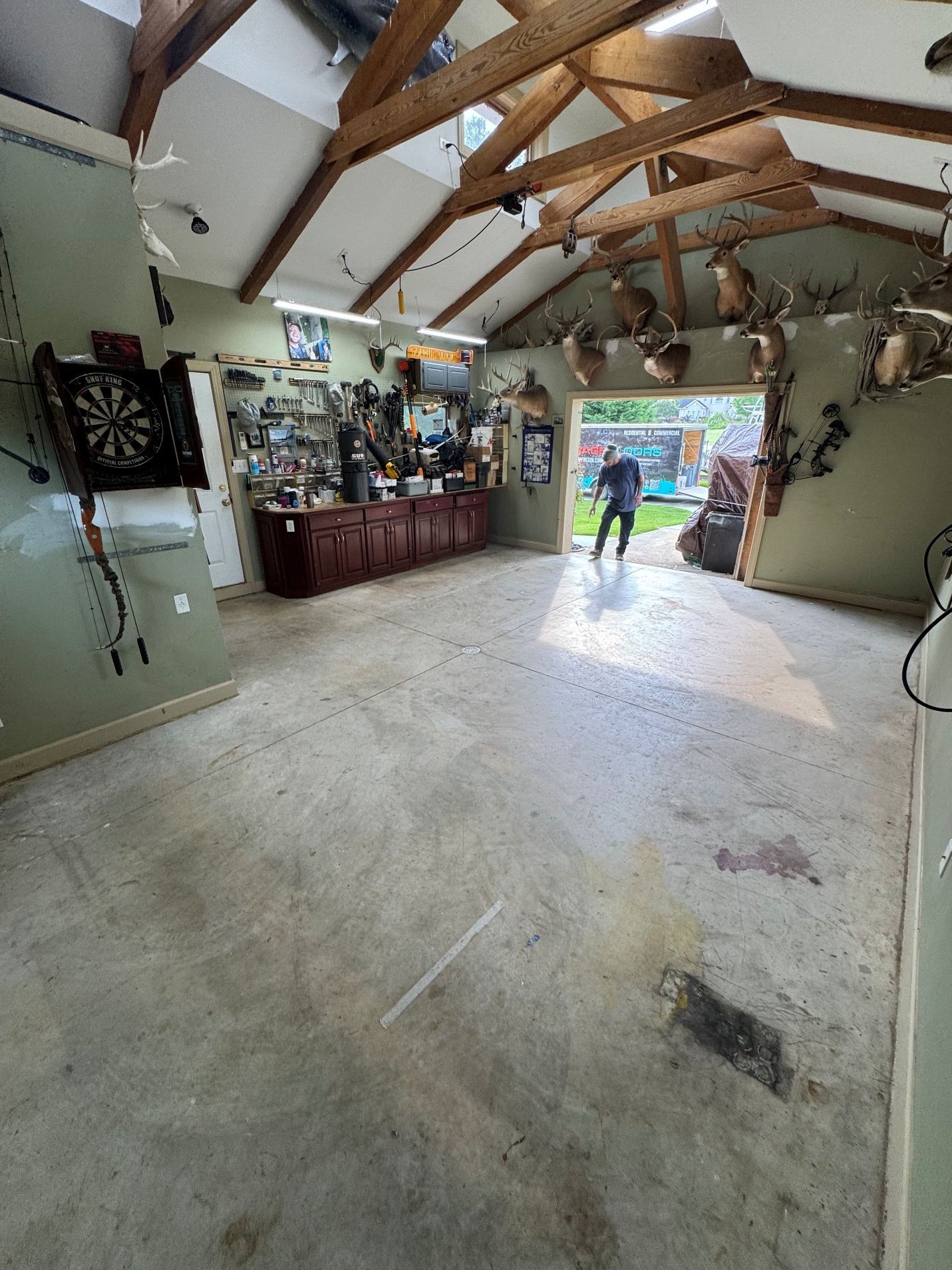 Spacious garage with dartboard, bar, open doors, and people visible outside.