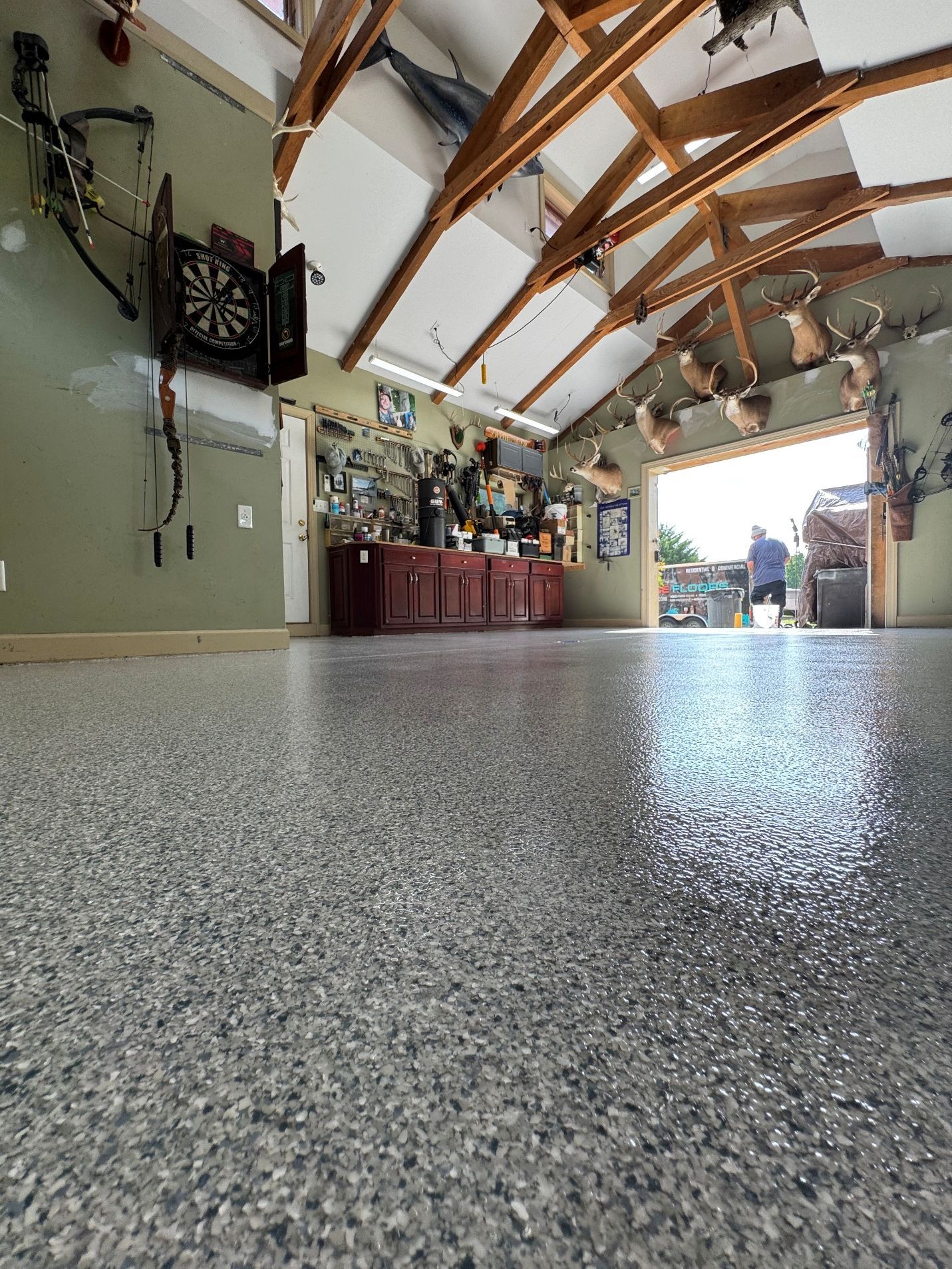 Spacious garage with a speckled floor, exposed wooden beams, and a workbench along the left wall.