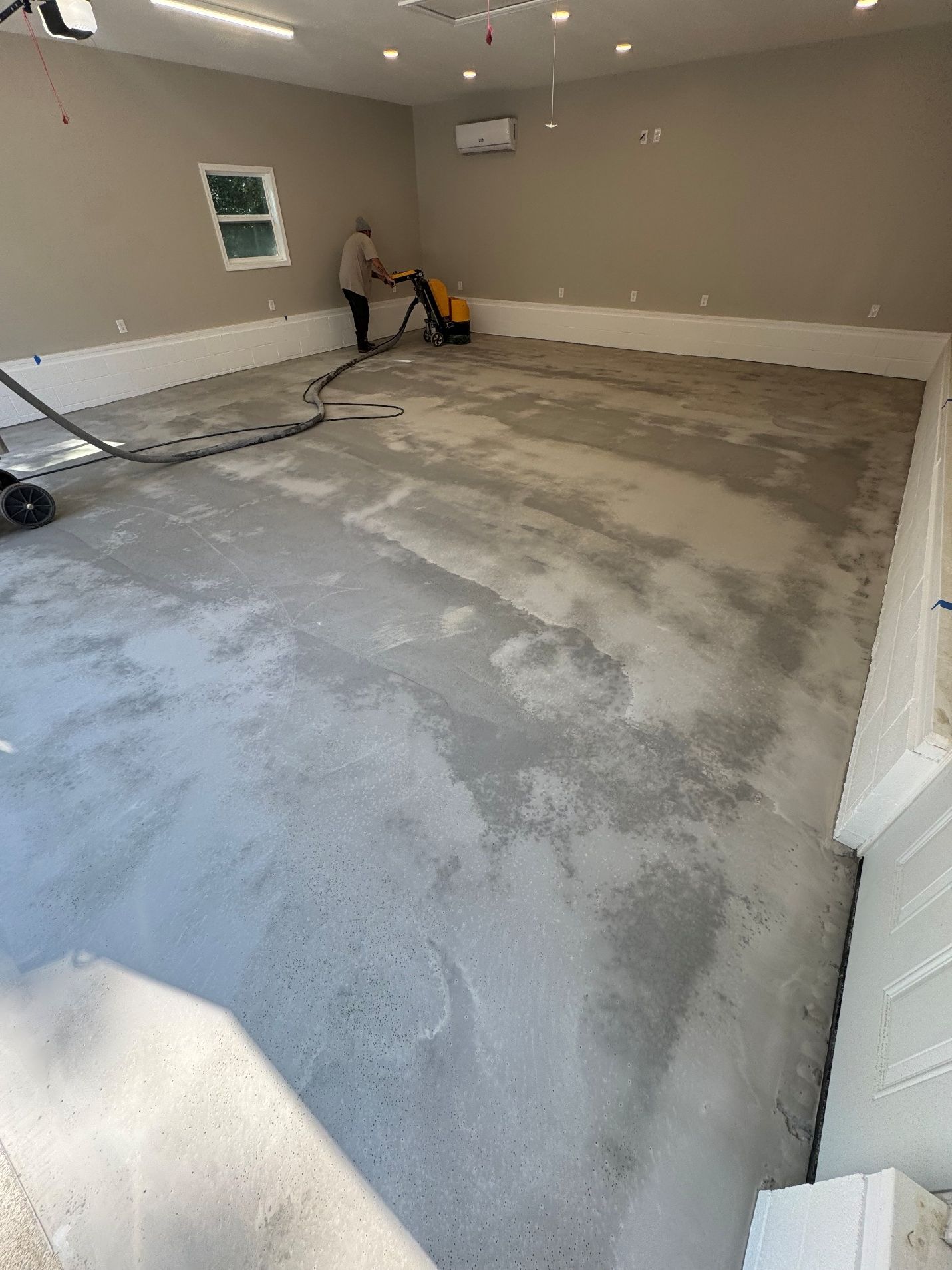 Empty unfinished garage with a concrete floor, gray walls, and a person using equipment near the back wall.