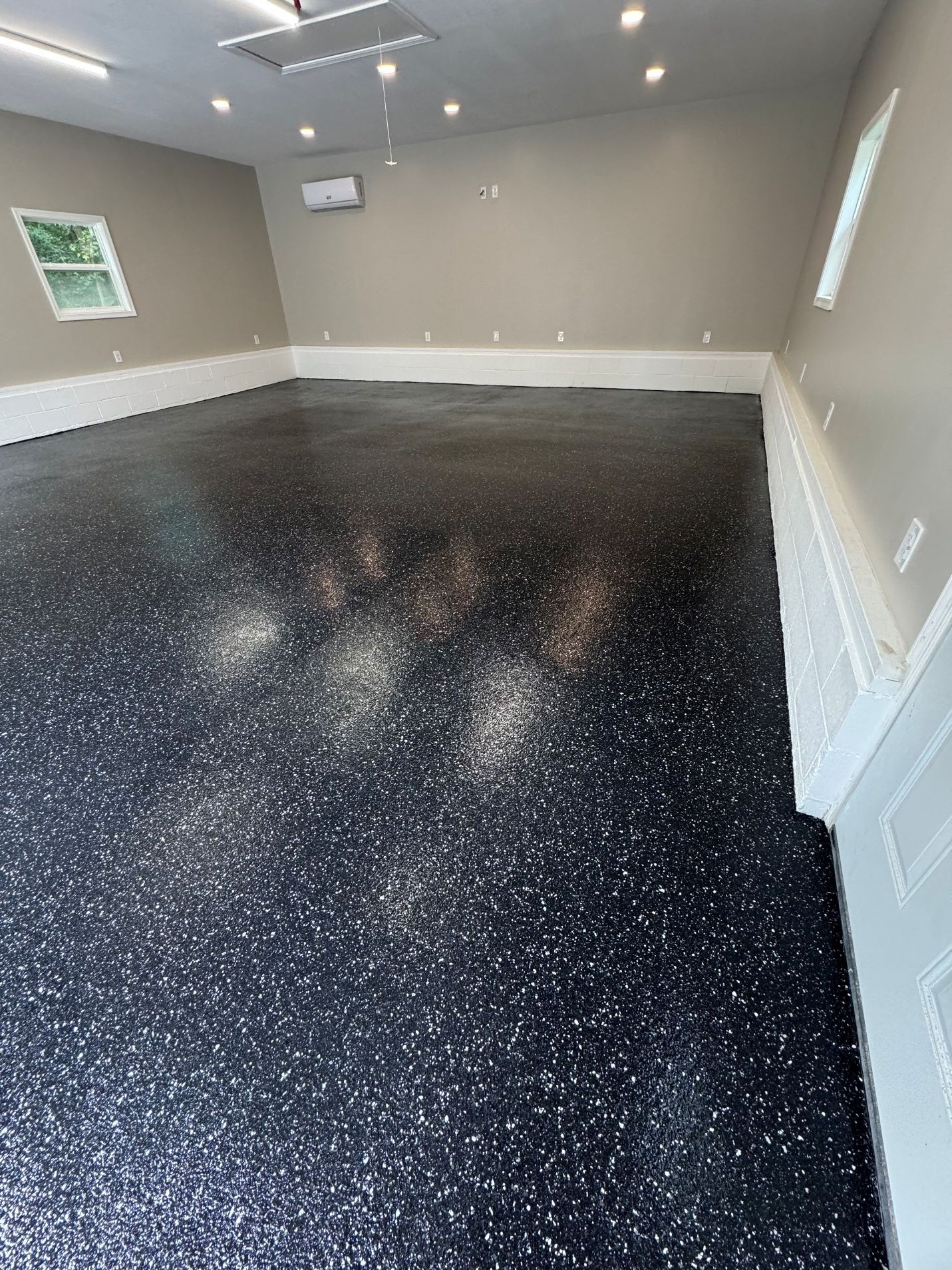 Empty gray room with black speckled epoxy floor and ceiling lights.