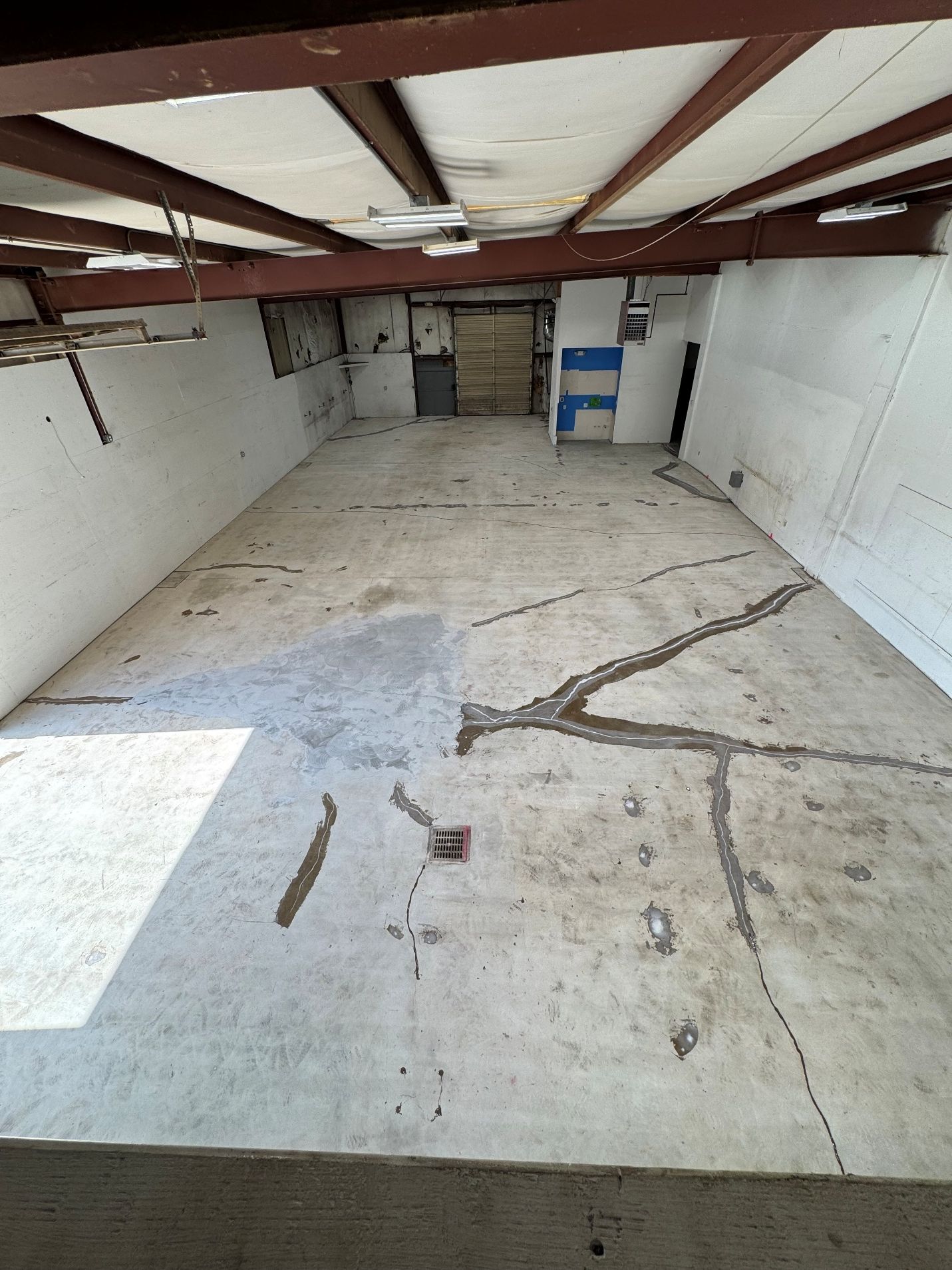 Empty unfinished basement with cracked concrete floor, exposed beams, and white walls.