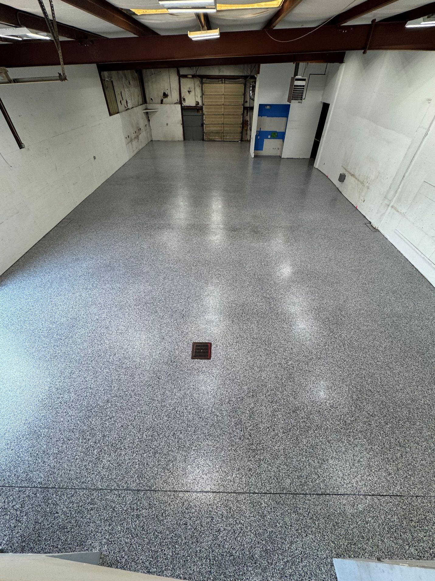 Empty white basement room with speckled gray floor and exposed ceiling beams.
