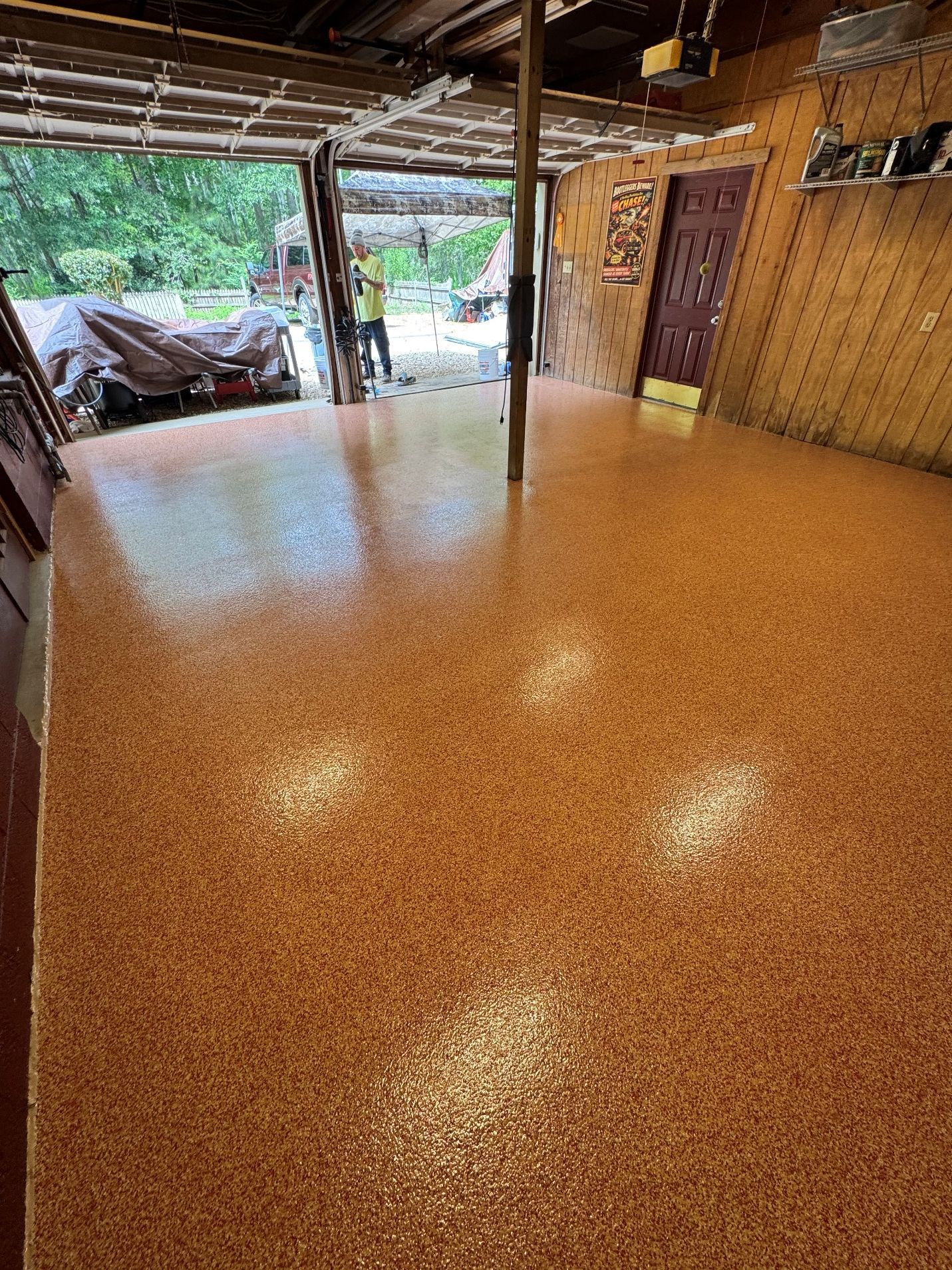 Open-air room with glossy orange-speckled floor, bamboo walls, and a view of greenery outside.