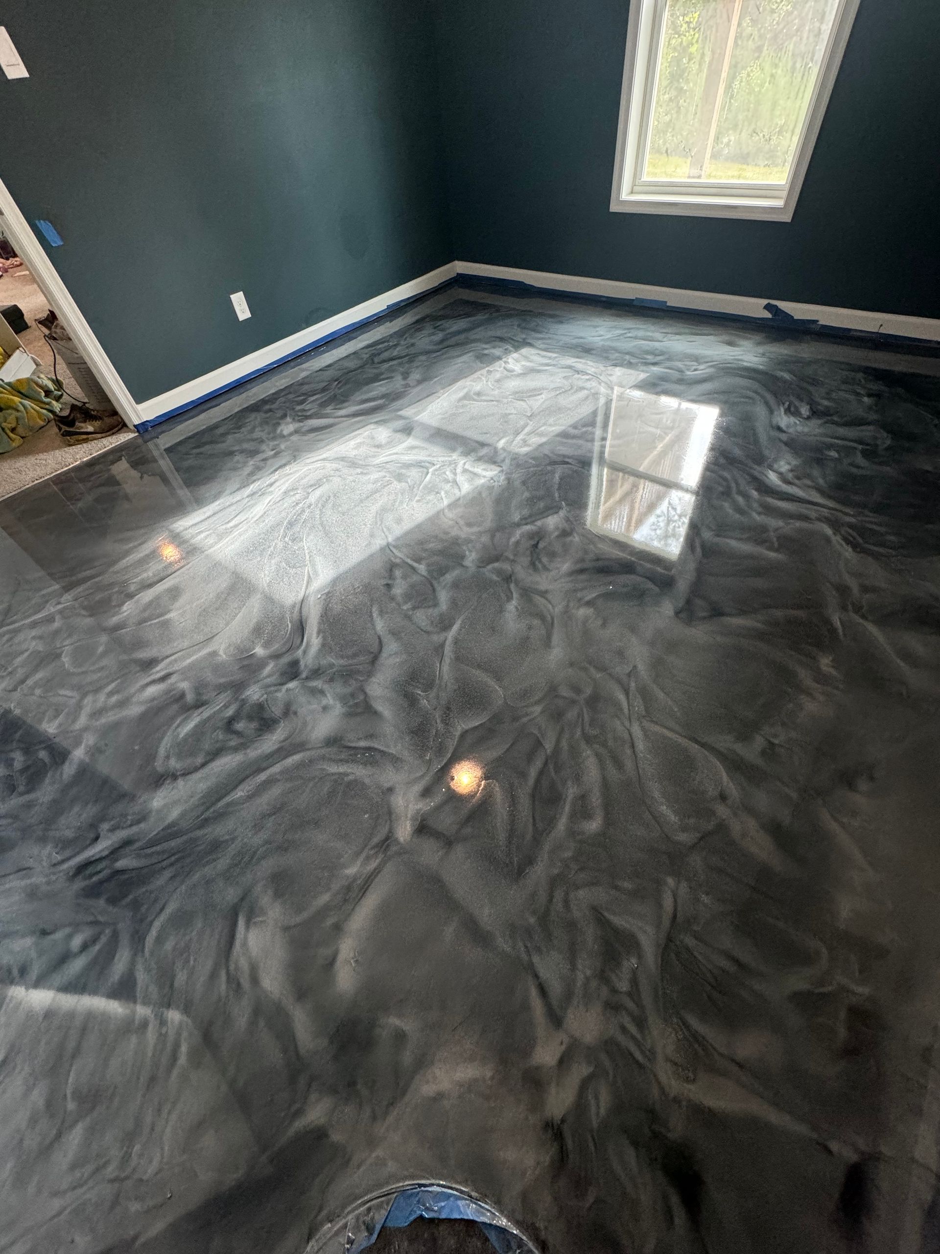 Empty room with dark walls and marbled black floor, lit by sunlight from a window.