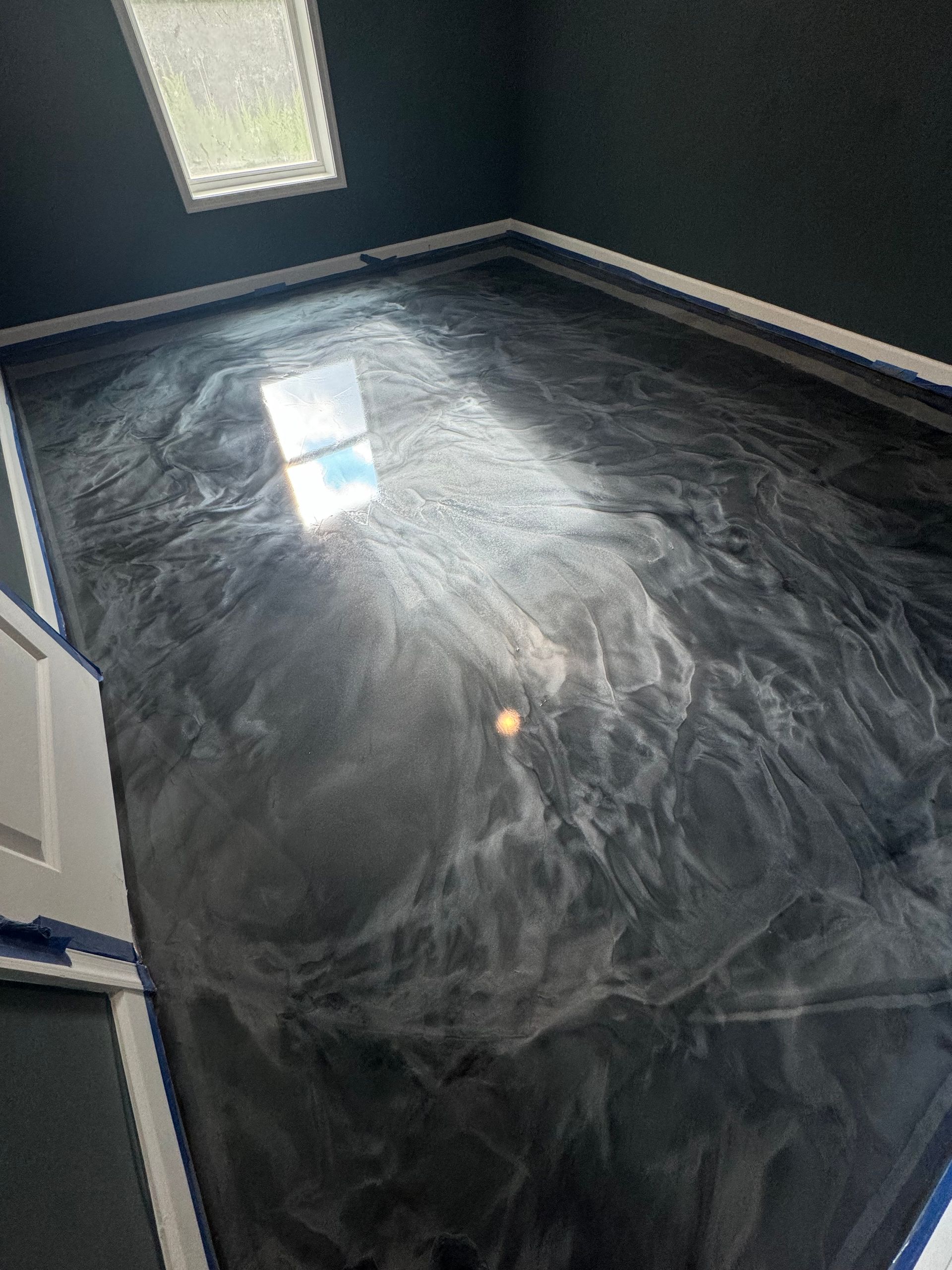 Dark room with a shiny black floor reflecting light from a window and ceiling panel.