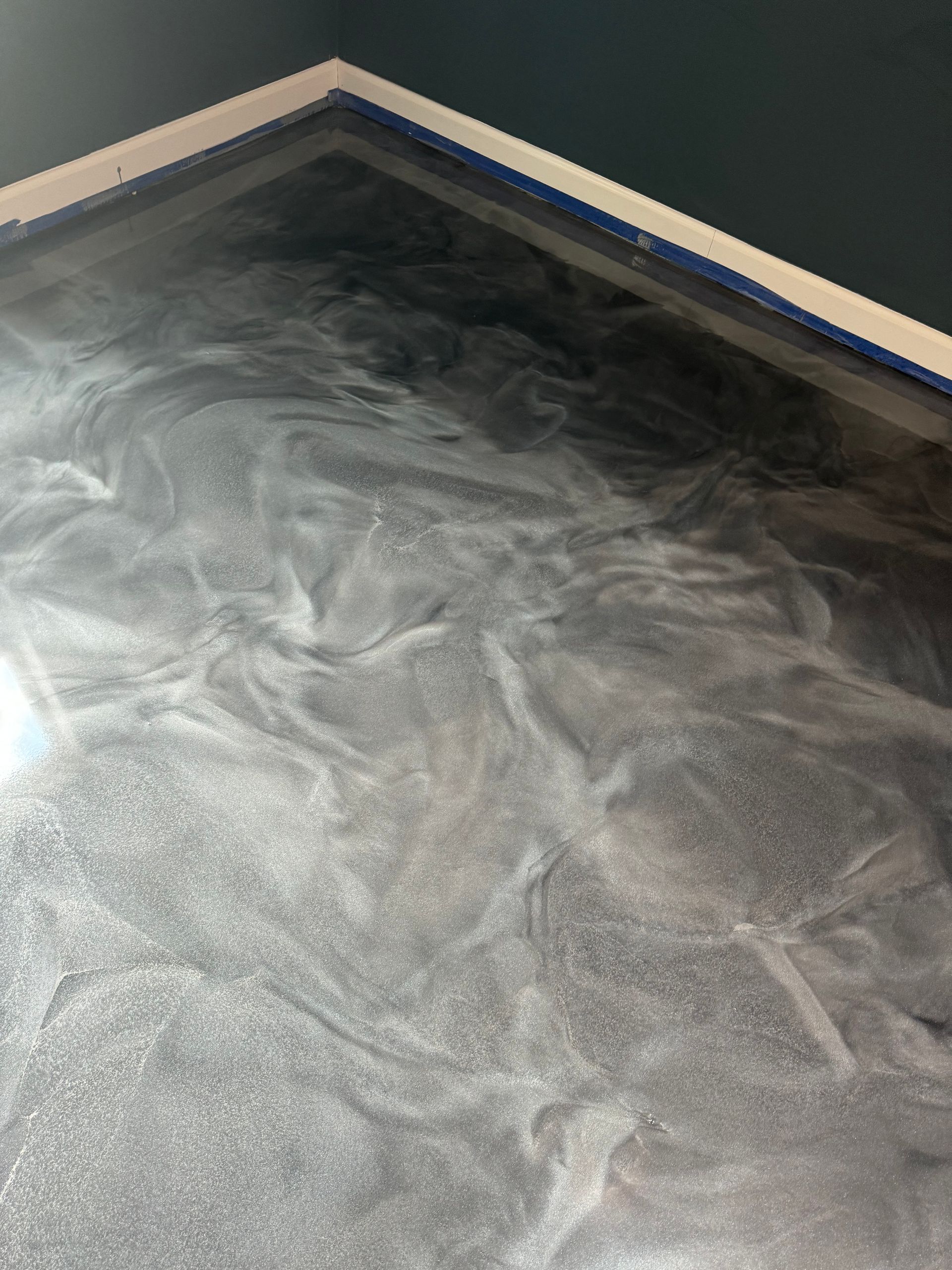 Dark gray floor with a white and blue corner trim, showing a swirled coating or dust pattern