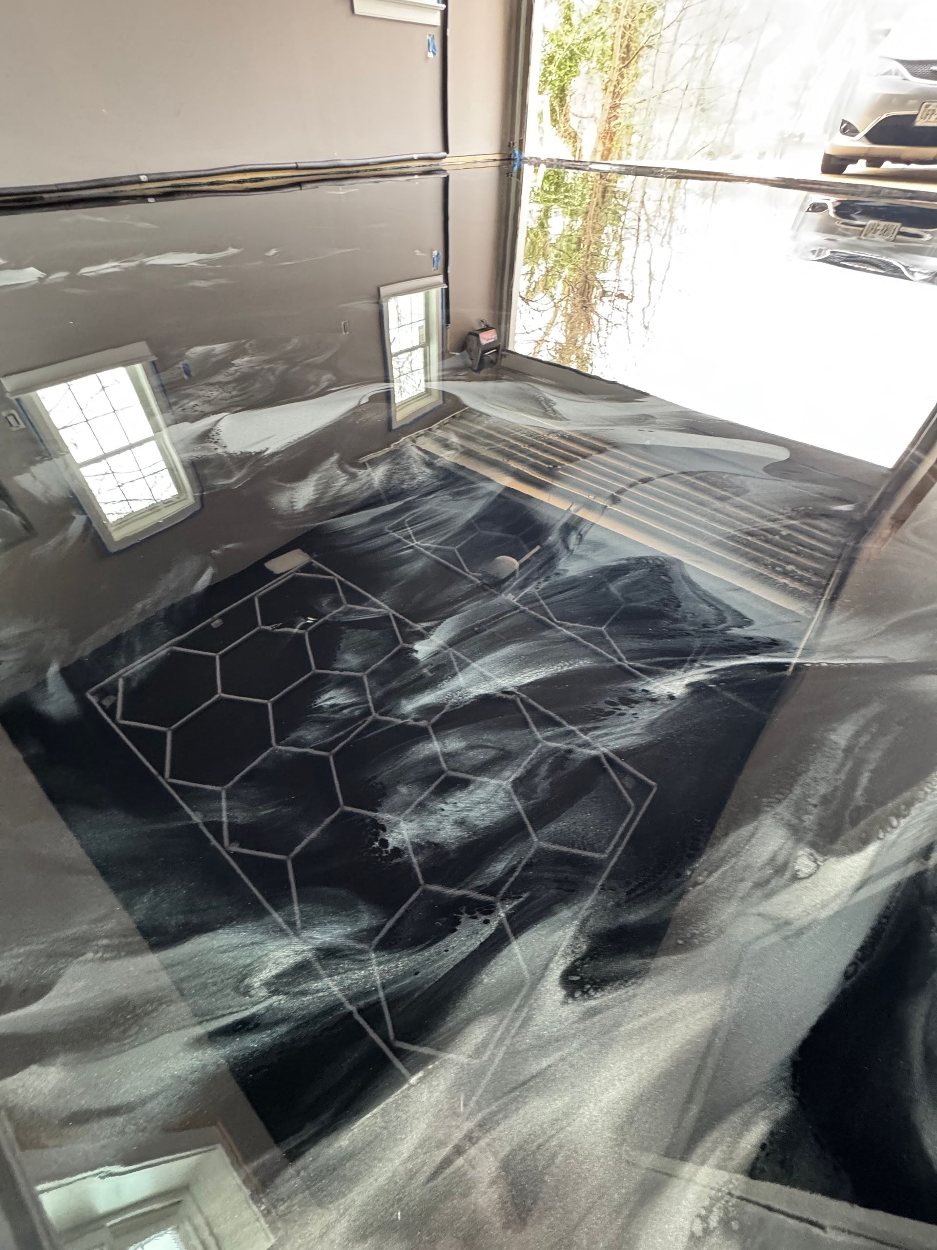Black bed with rumpled white sheets in a bright bedroom, near windows and a mirrored wall.