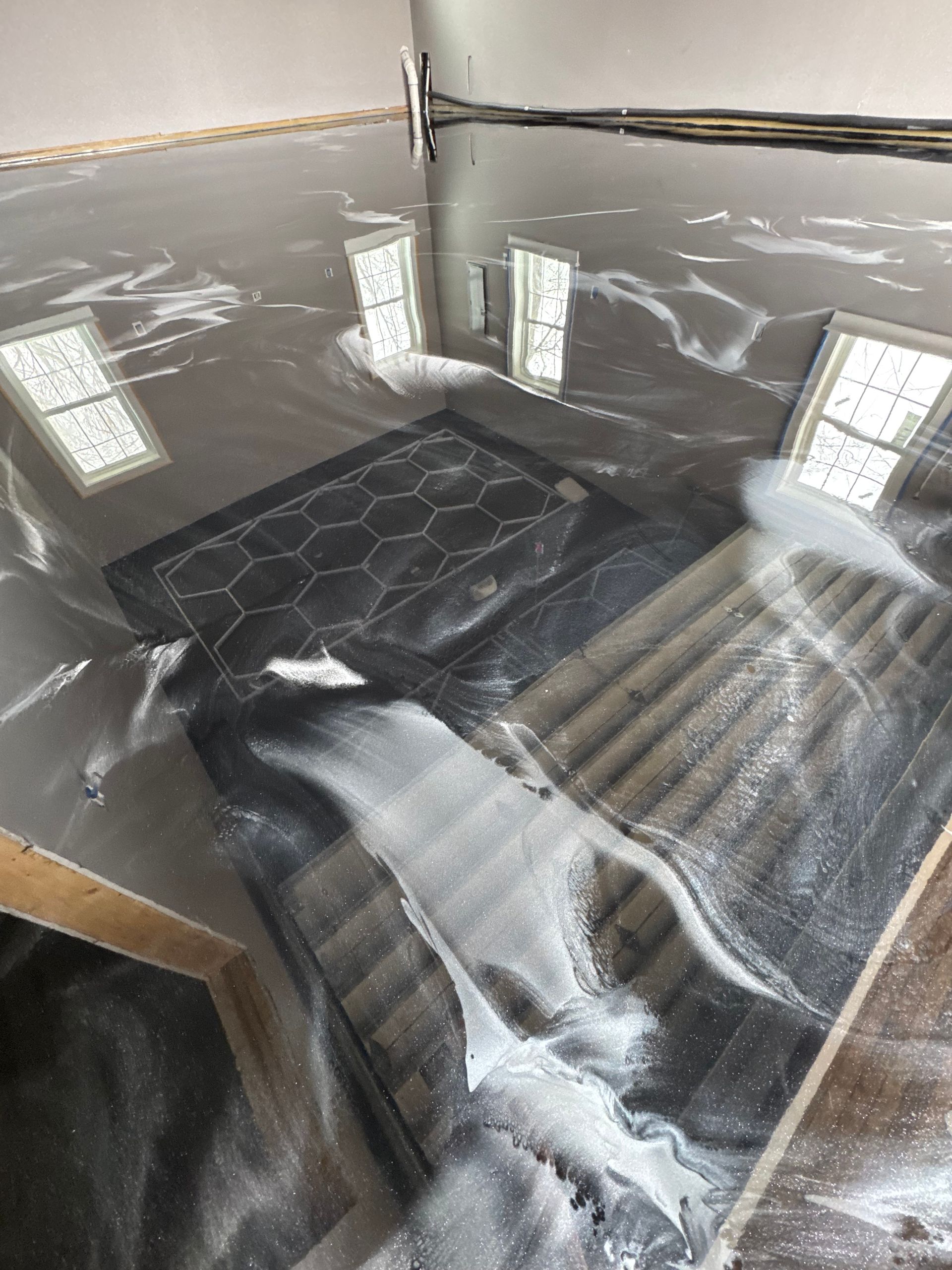 Black mattress on a tiled floor in a sunlit room, with bright window reflections on glossy walls.