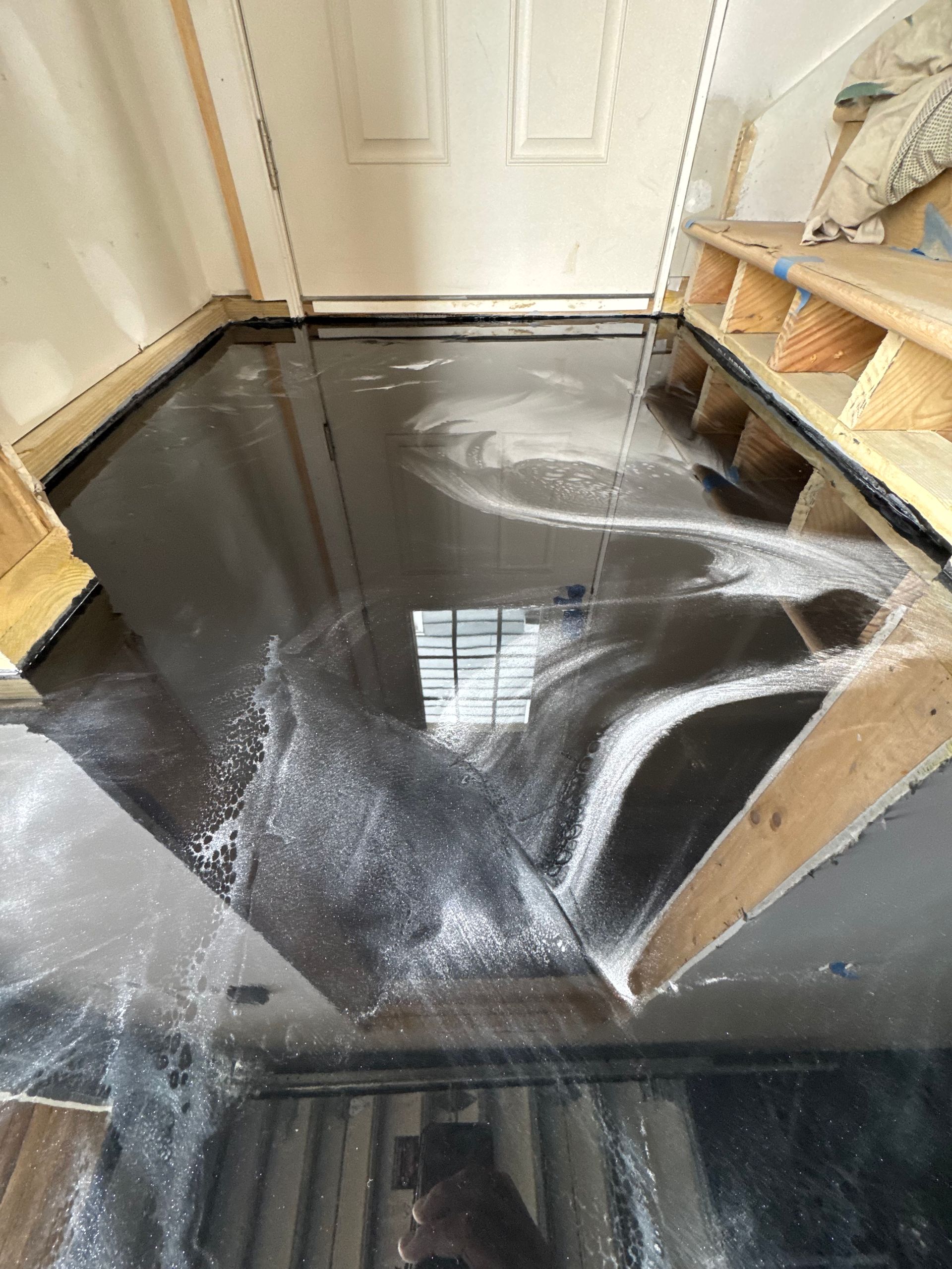 Flooded hallway with standing dark water and white foam near a closed door and shelving unit