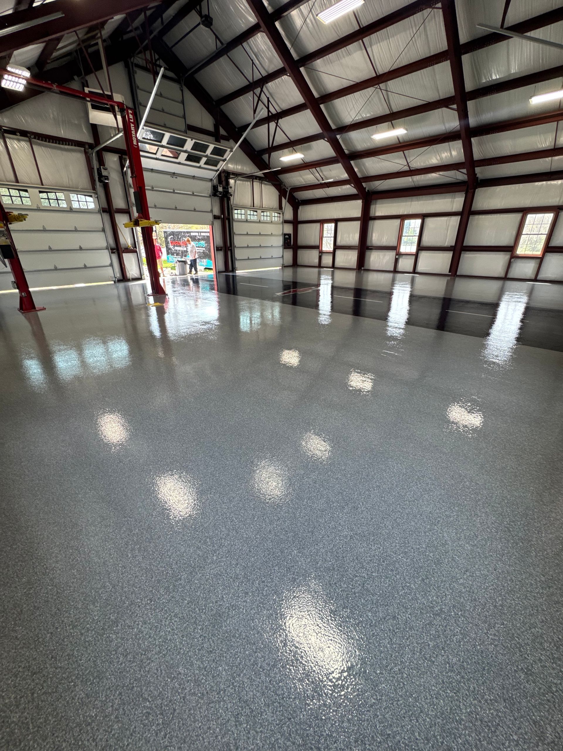 Empty industrial warehouse with polished speckled floor, metal beams, and overhead lights reflected on the ground
