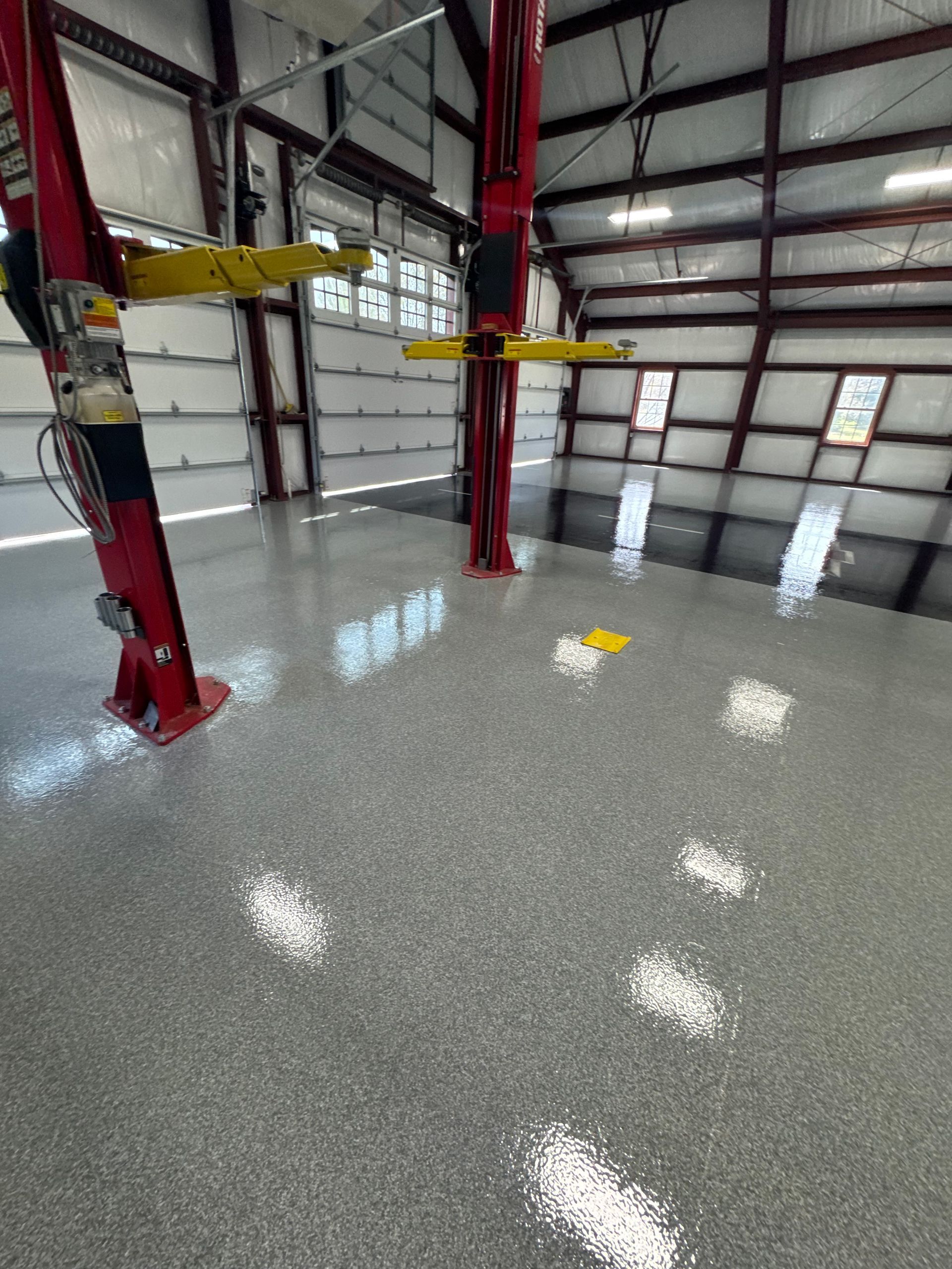 Empty industrial warehouse with red steel columns, yellow beams, and a glossy concrete floor.