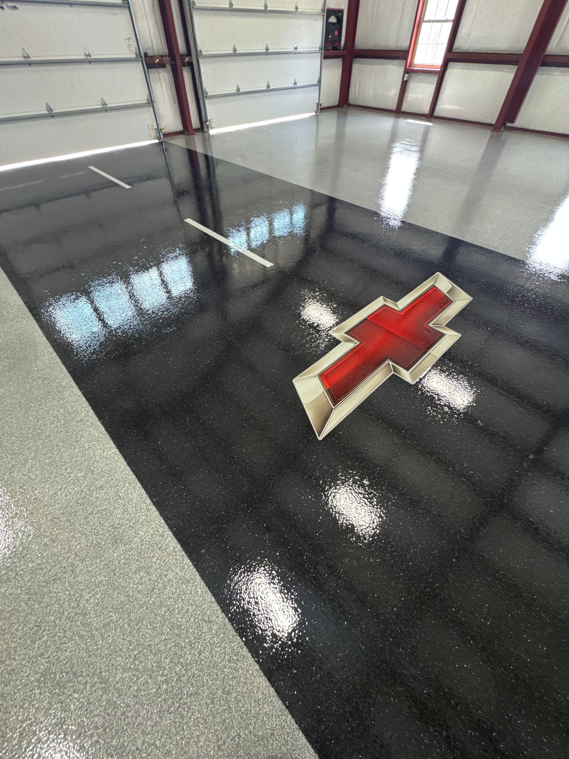 Shiny black garage floor with a red Chevrolet bowtie logo, reflecting overhead lights.