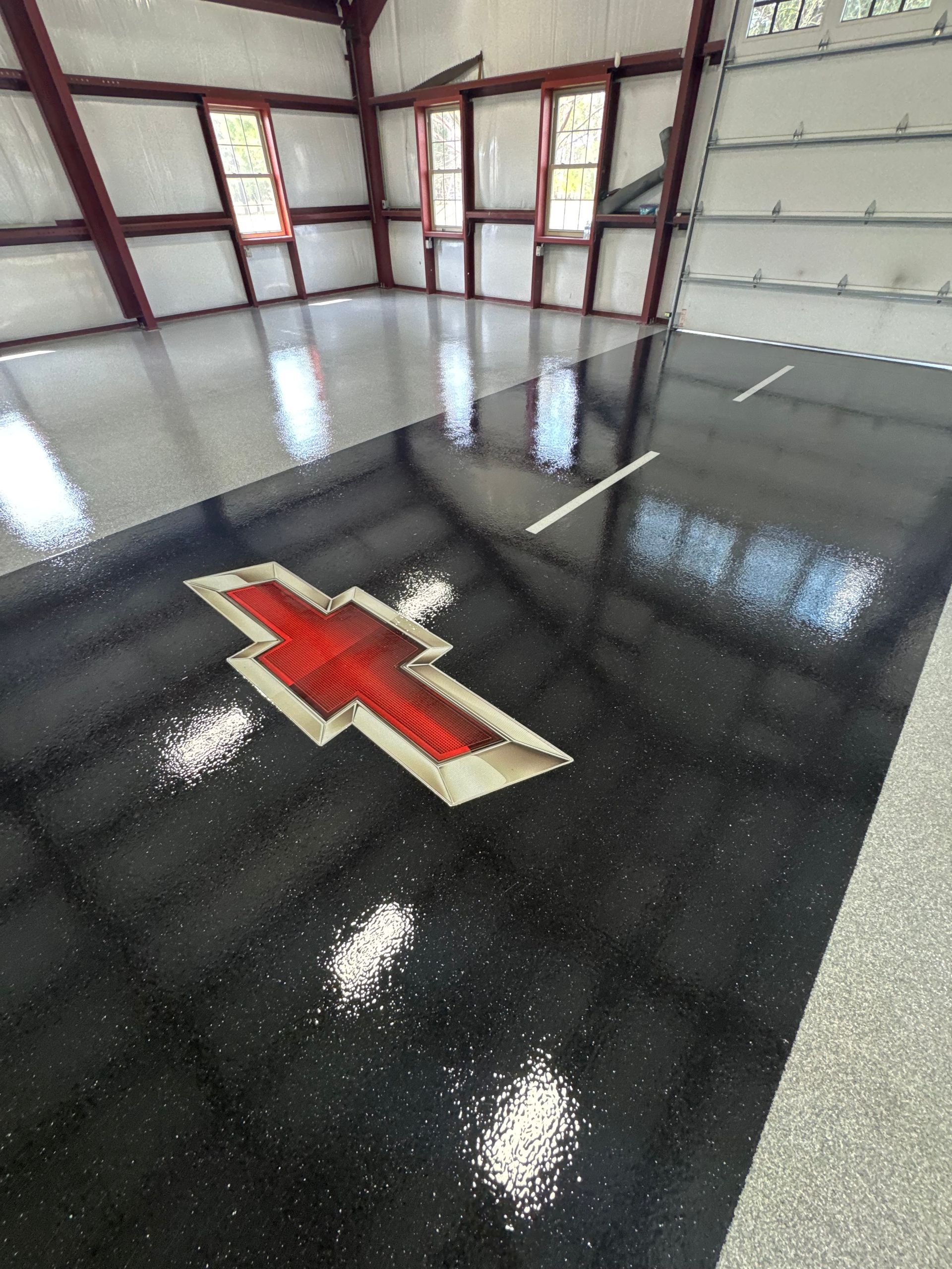 Shiny garage floor with a red Chevrolet bowtie logo and reflections of windows on the walls.