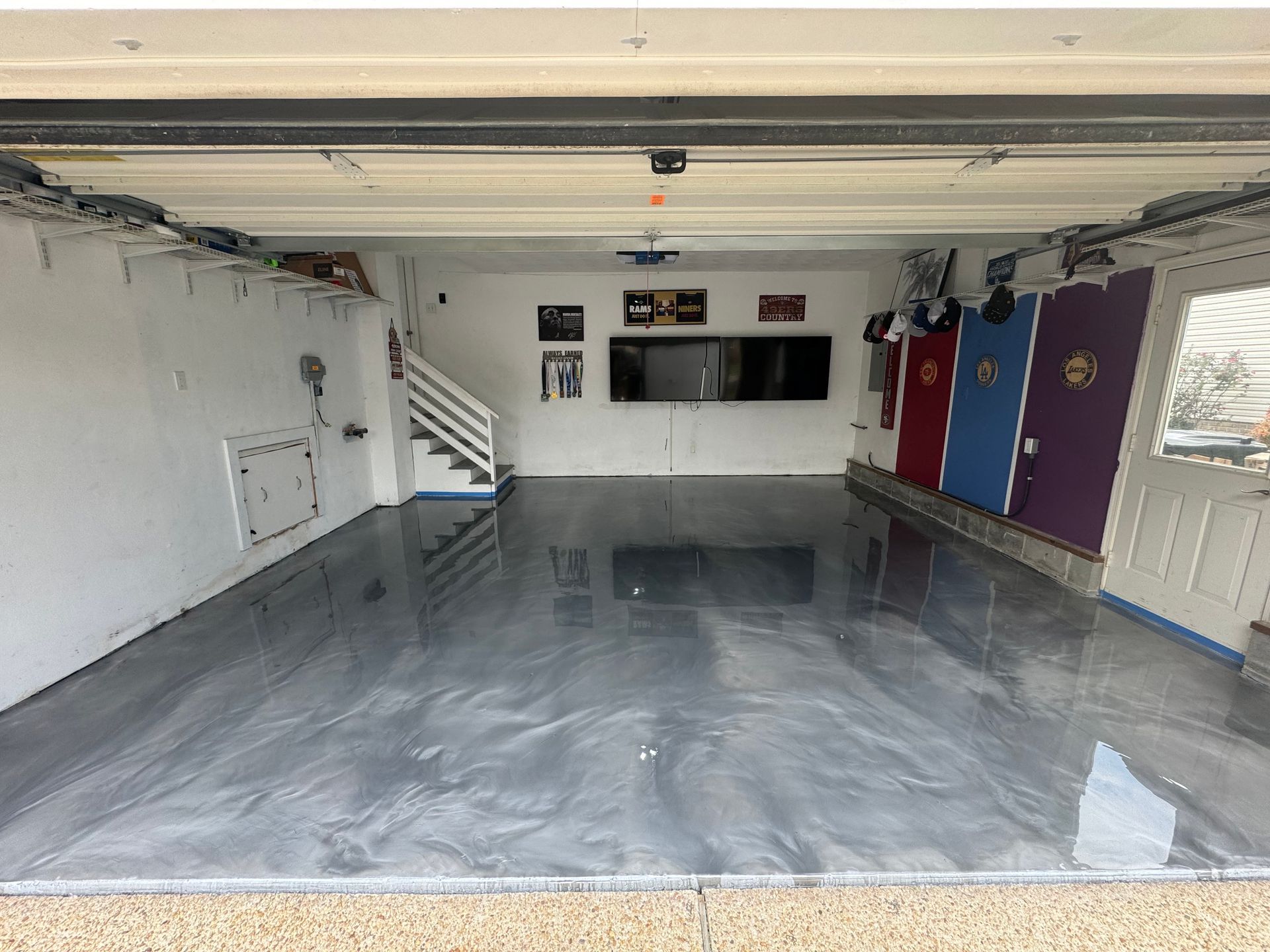 Empty garage-like room with glossy gray floor, white walls, stairs left, and colorful doors on the right.