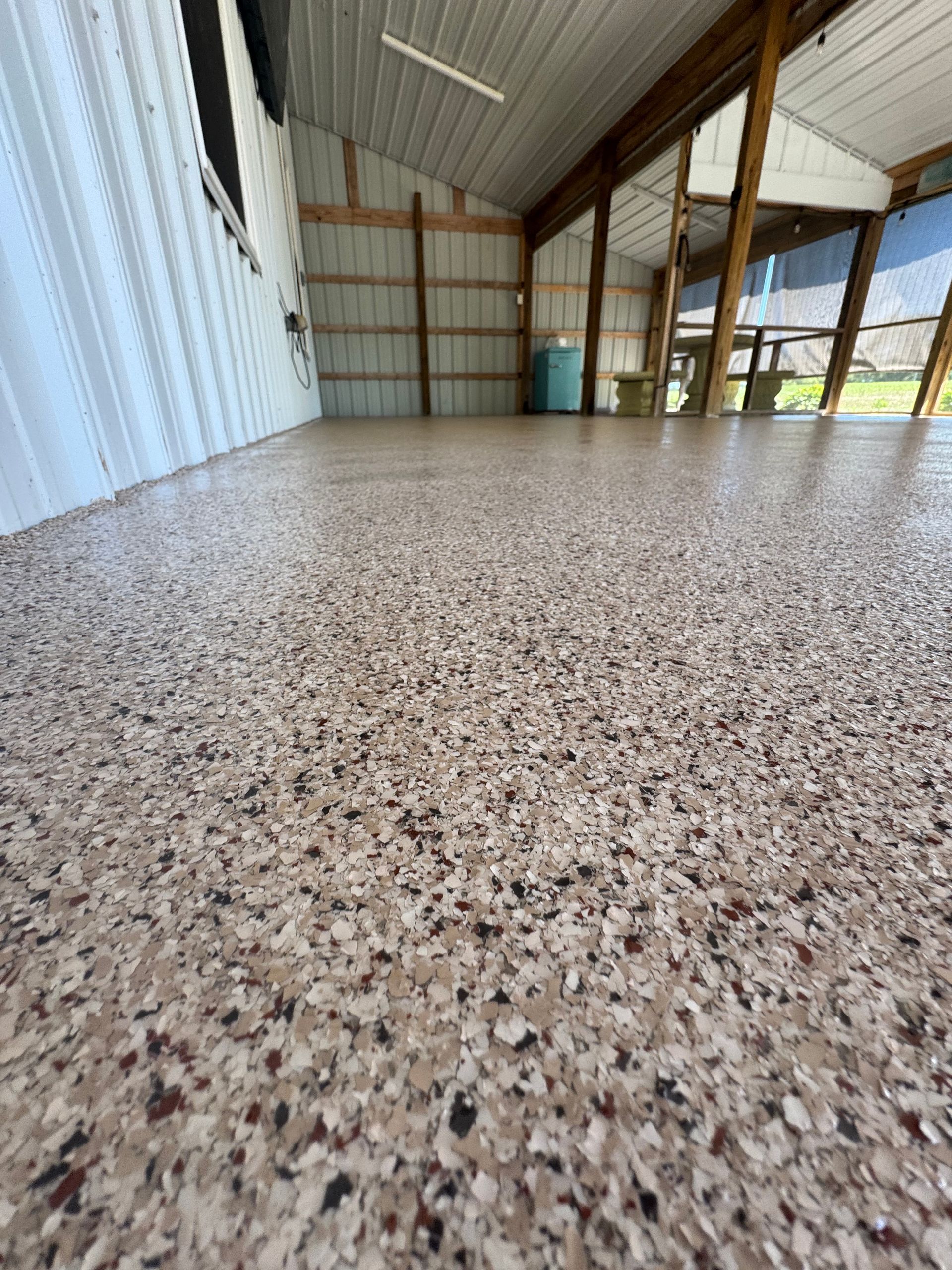 Empty covered porch with speckled floor, corrugated metal wall, and open view to a grassy yard.