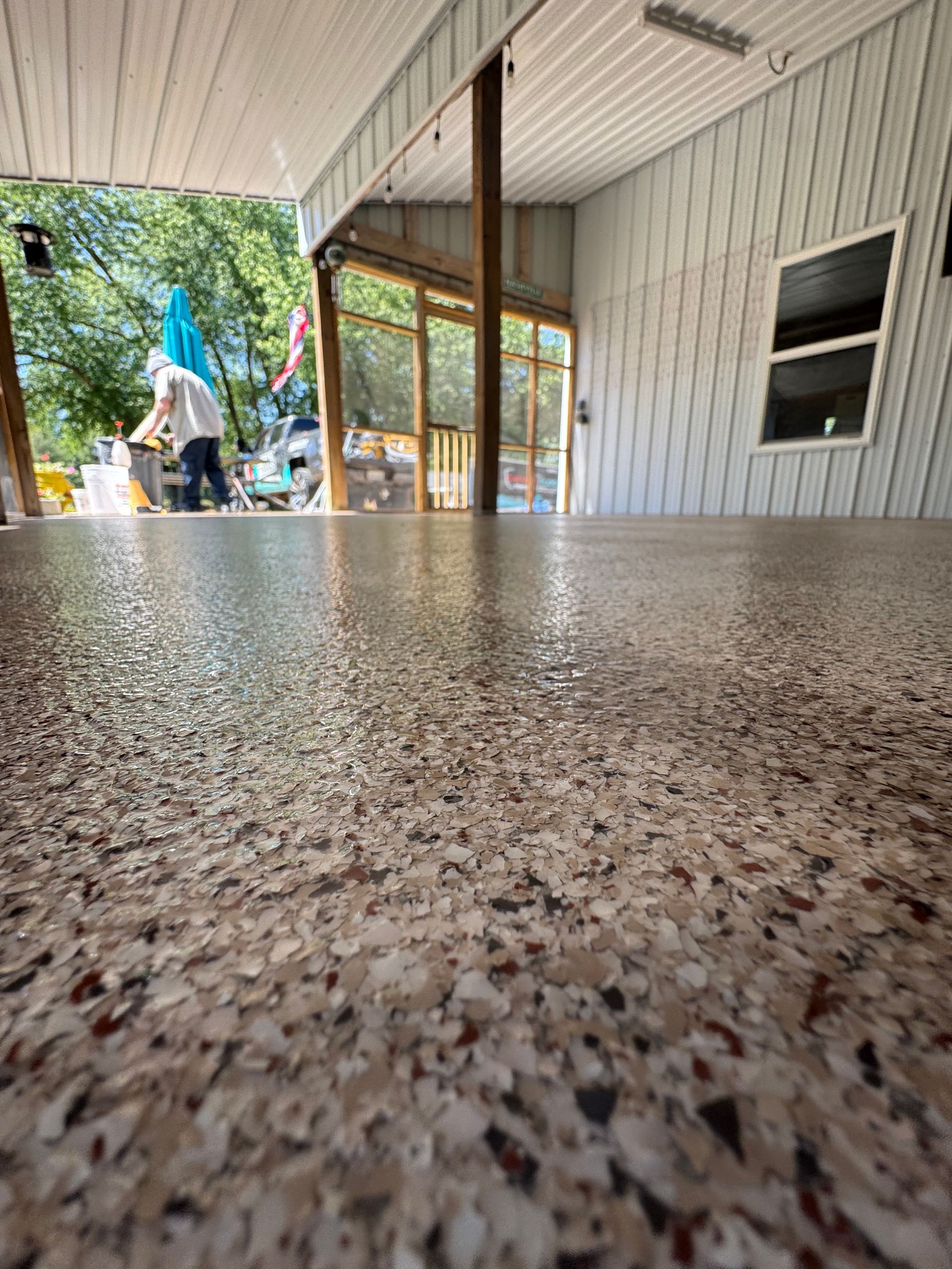 Low-angle view of a speckled countertop under a covered patio, with a person and outdoor yard in the background
