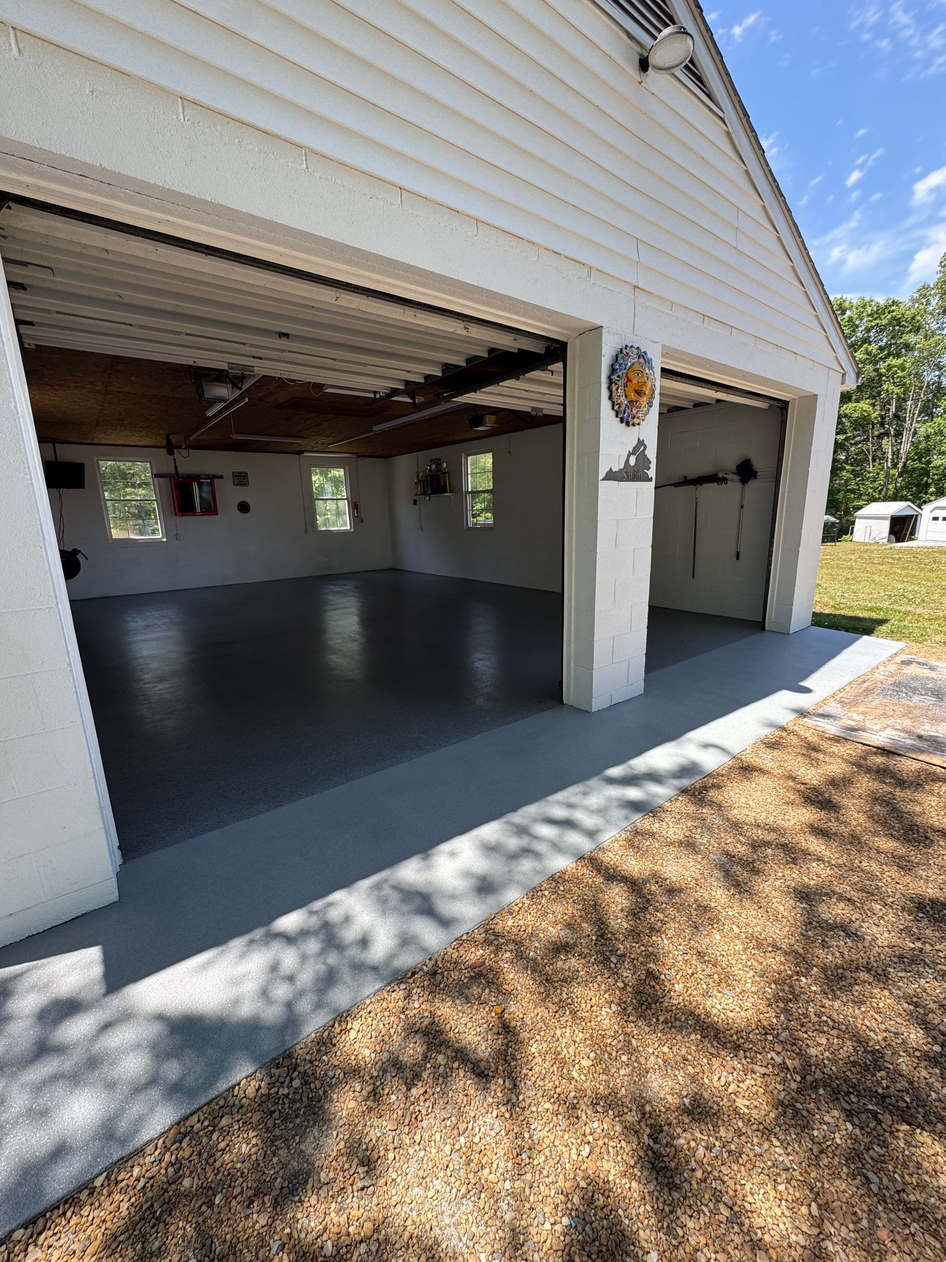 Open garage with gray epoxy floor, white siding, and a mounted sign beside the door.