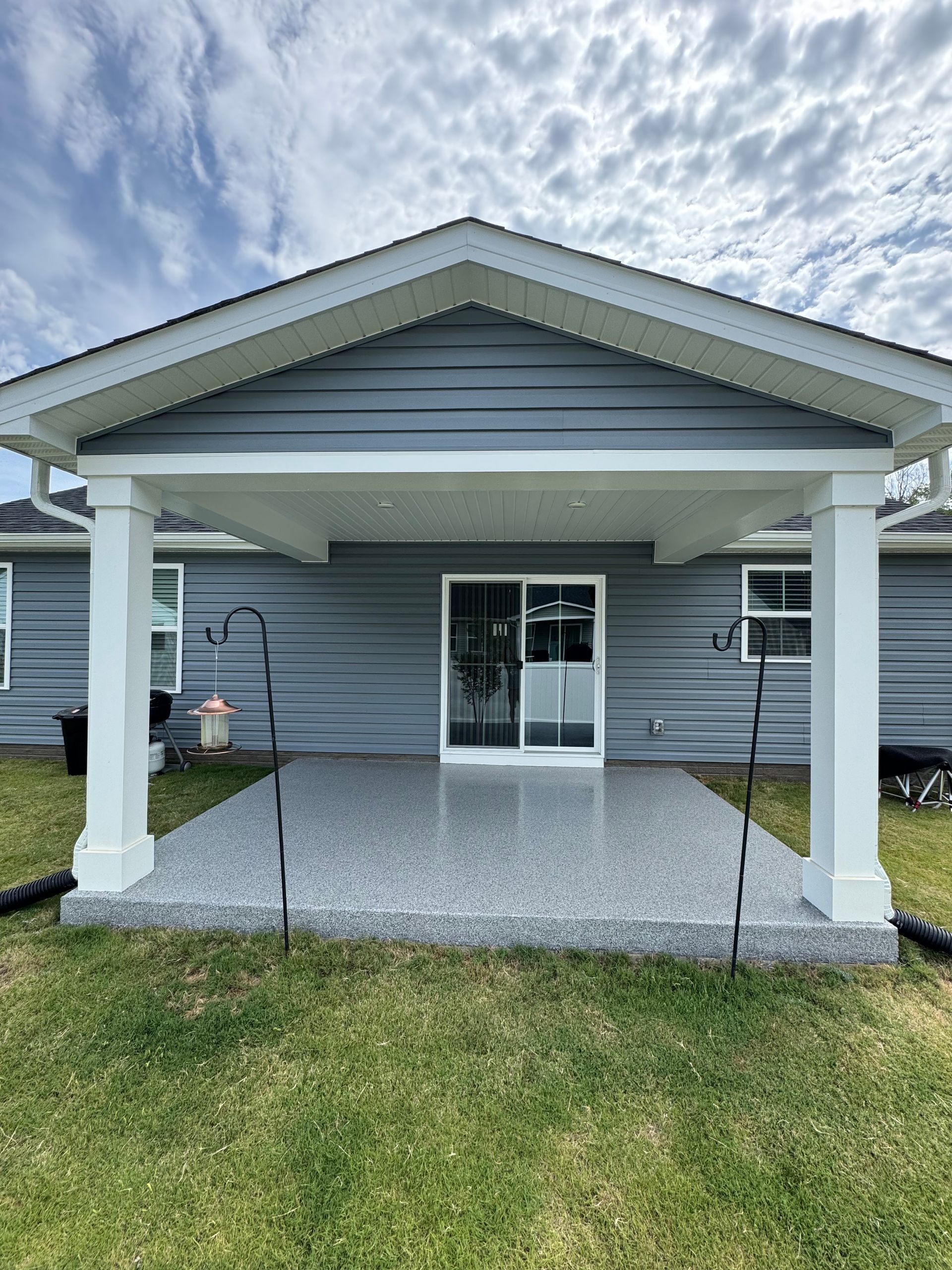 Front porch with white columns, gray siding, and a glass double door under a gabled roof.