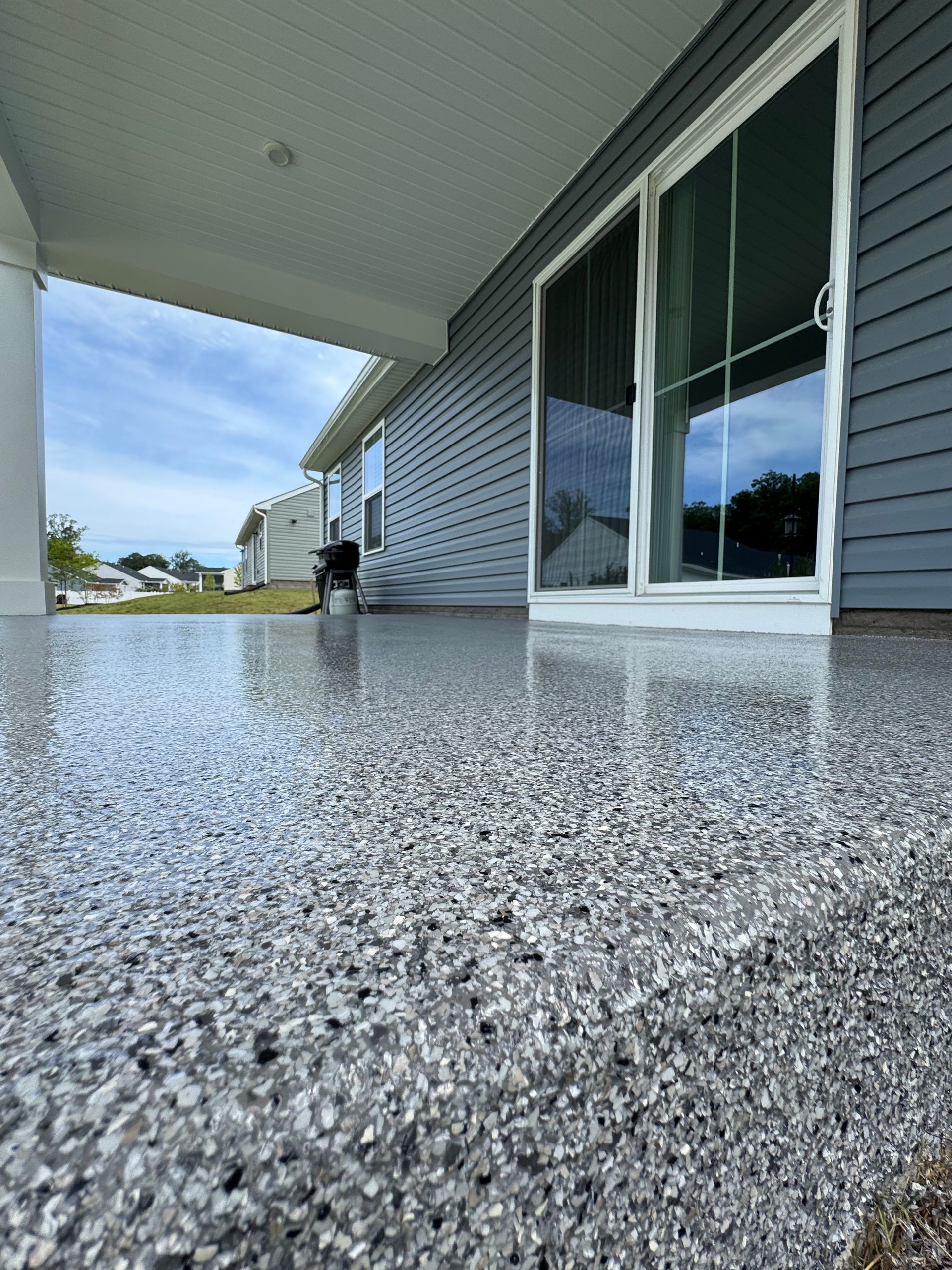 Covered porch with speckled concrete floor, sliding glass doors, and a person in the distance.