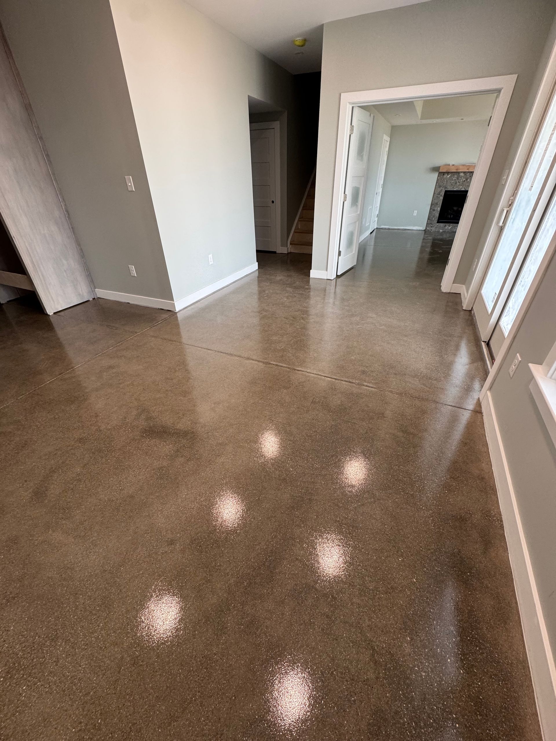Empty hallway with glossy brown floor, white walls, and an open doorway leading to another room