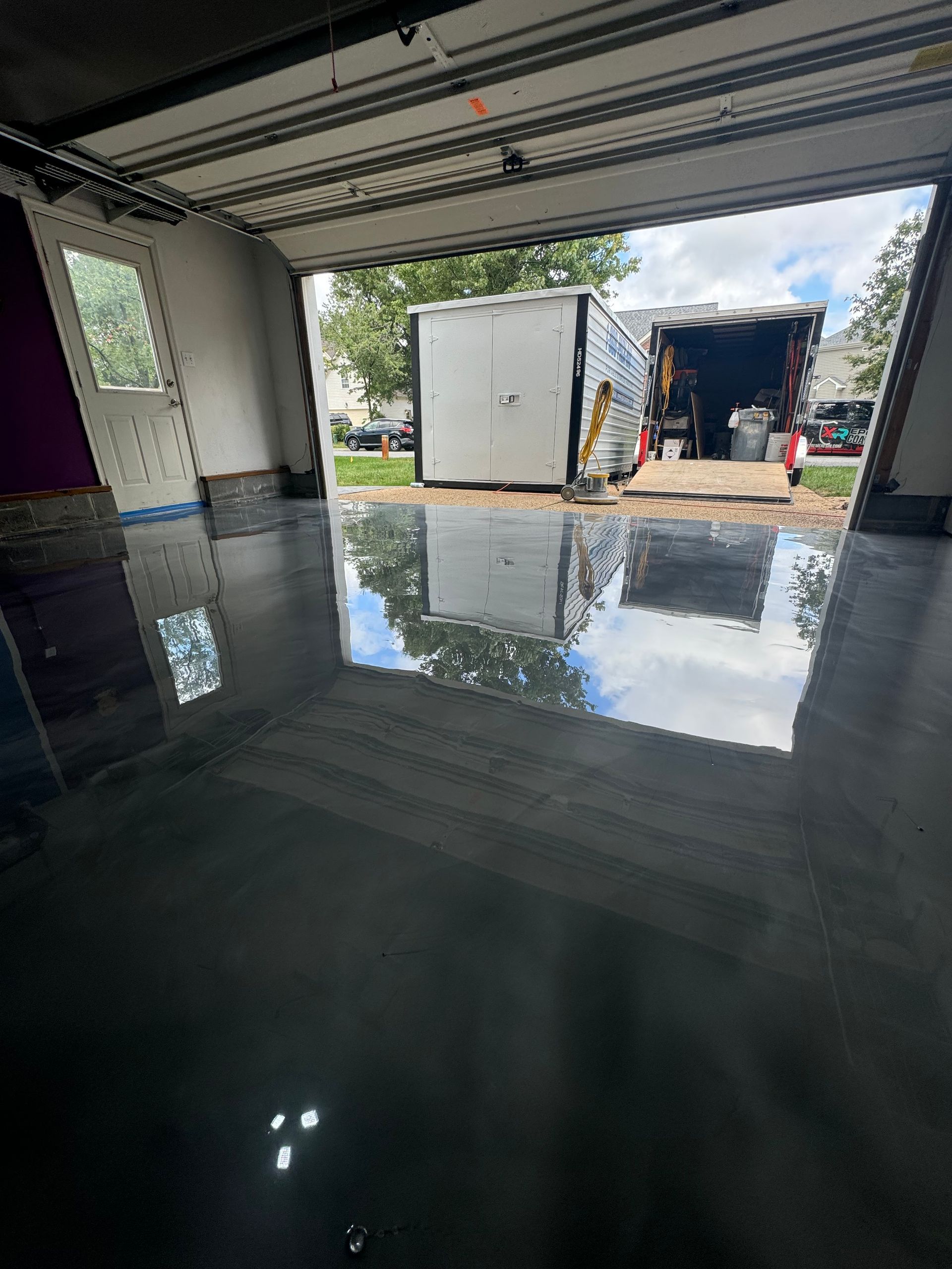 Flooded garage interior with reflective water and an open doorway showing equipment outside