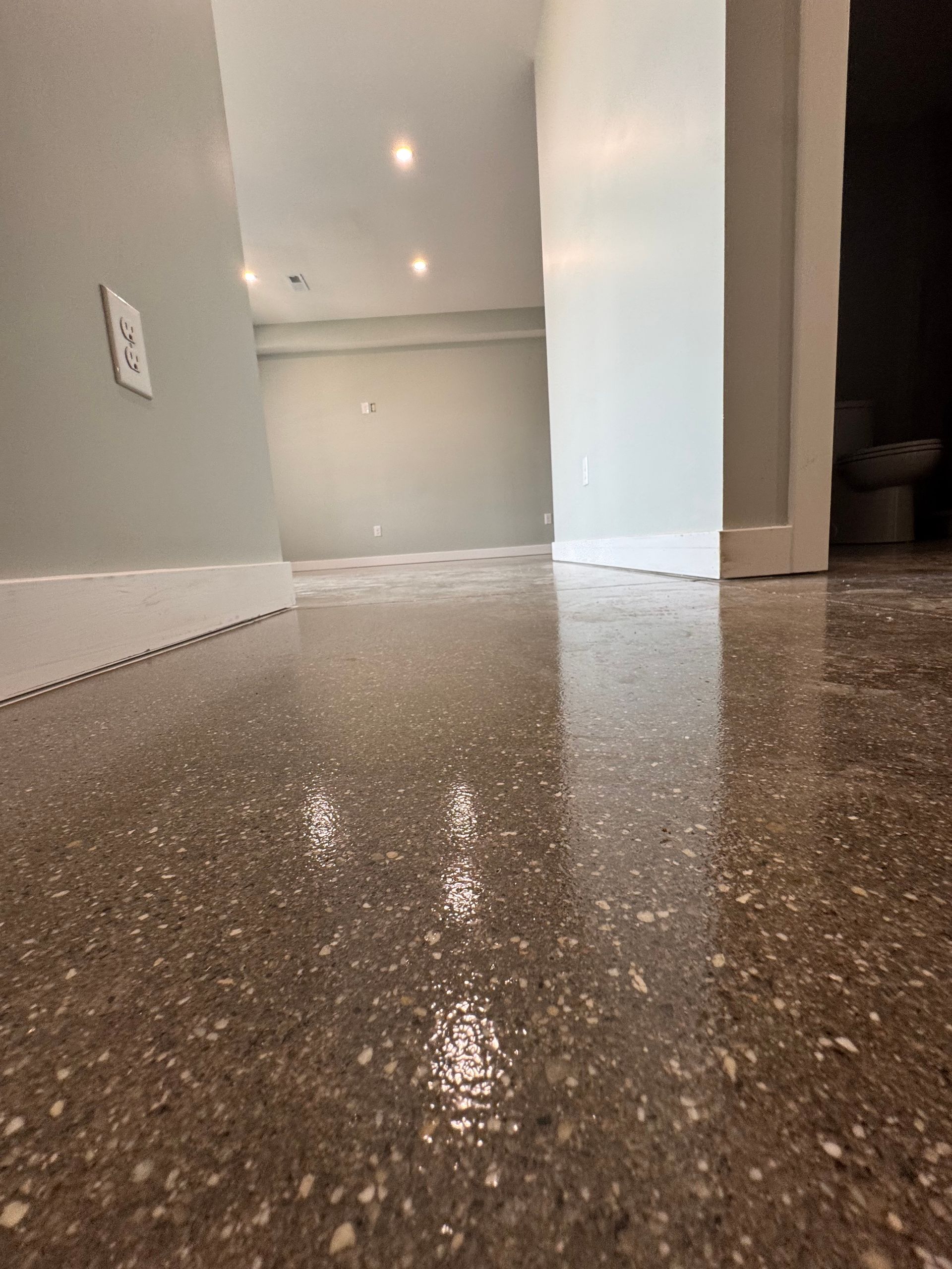 Low-angle view of a speckled terrazzo floor in a bright hallway with white walls and recessed lights.